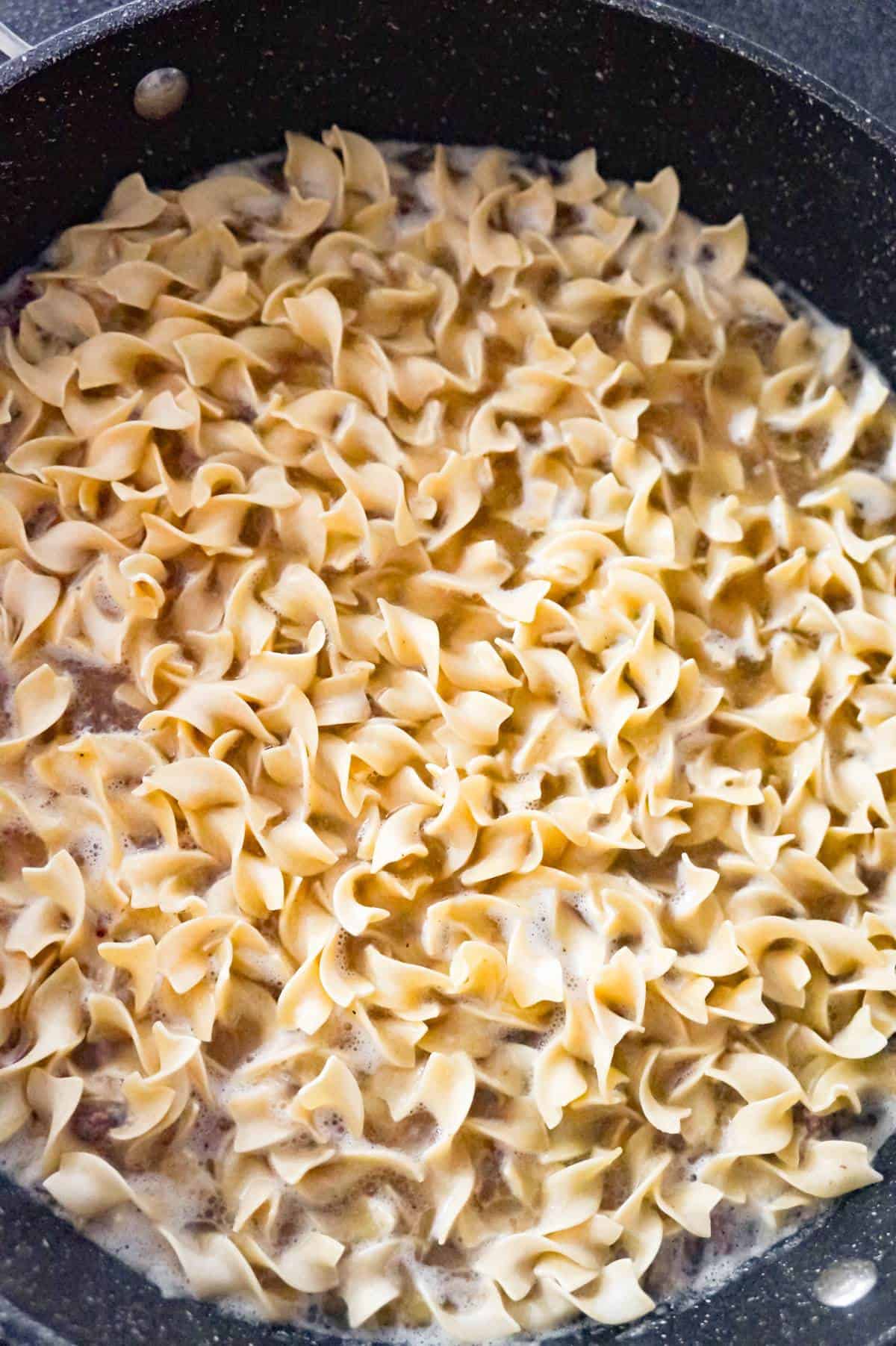 uncooked egg noodles in a pan with cooked ground beef