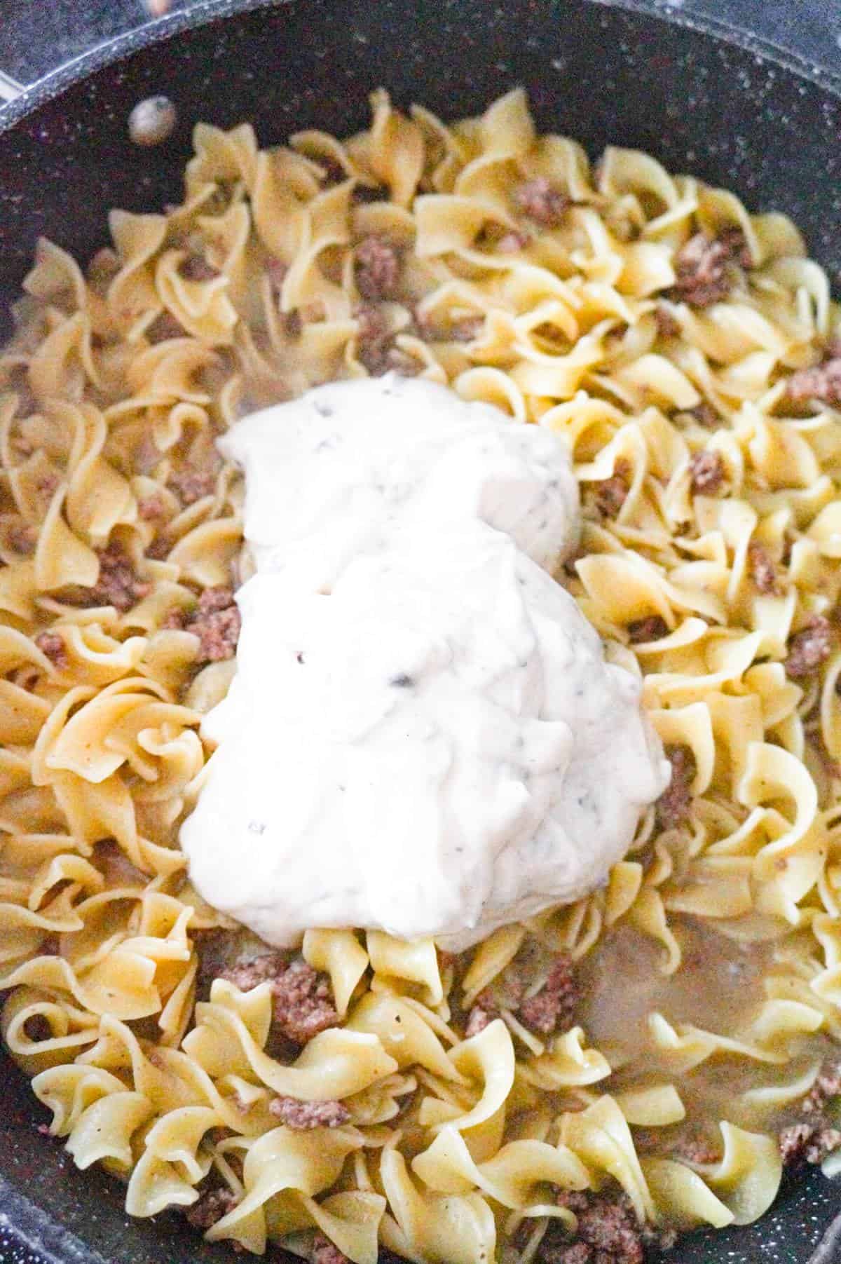 condensed cream of mushroom soup on top of cooked egg noodles and ground beef in a pan