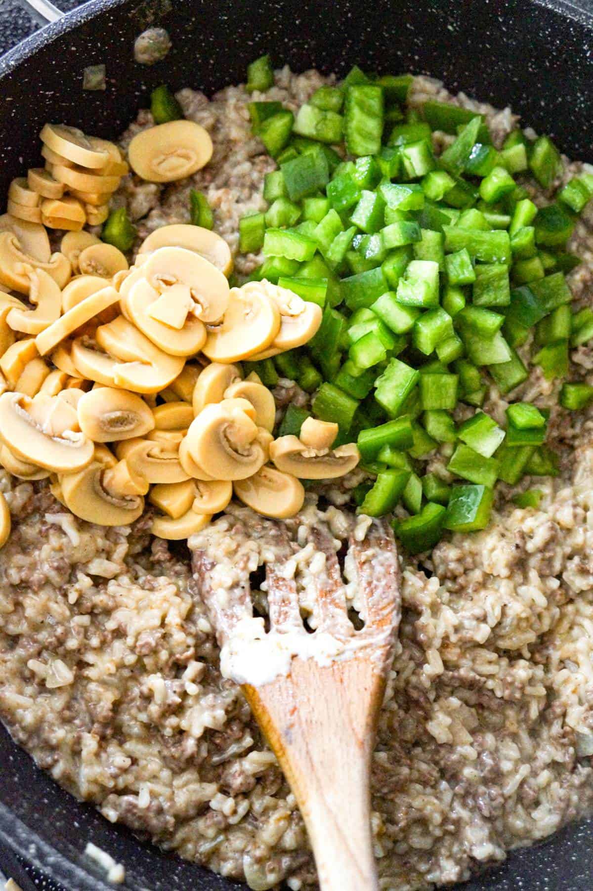 sliced mushrooms and diced green peppers on top of ground beef and rice mixture in a pan