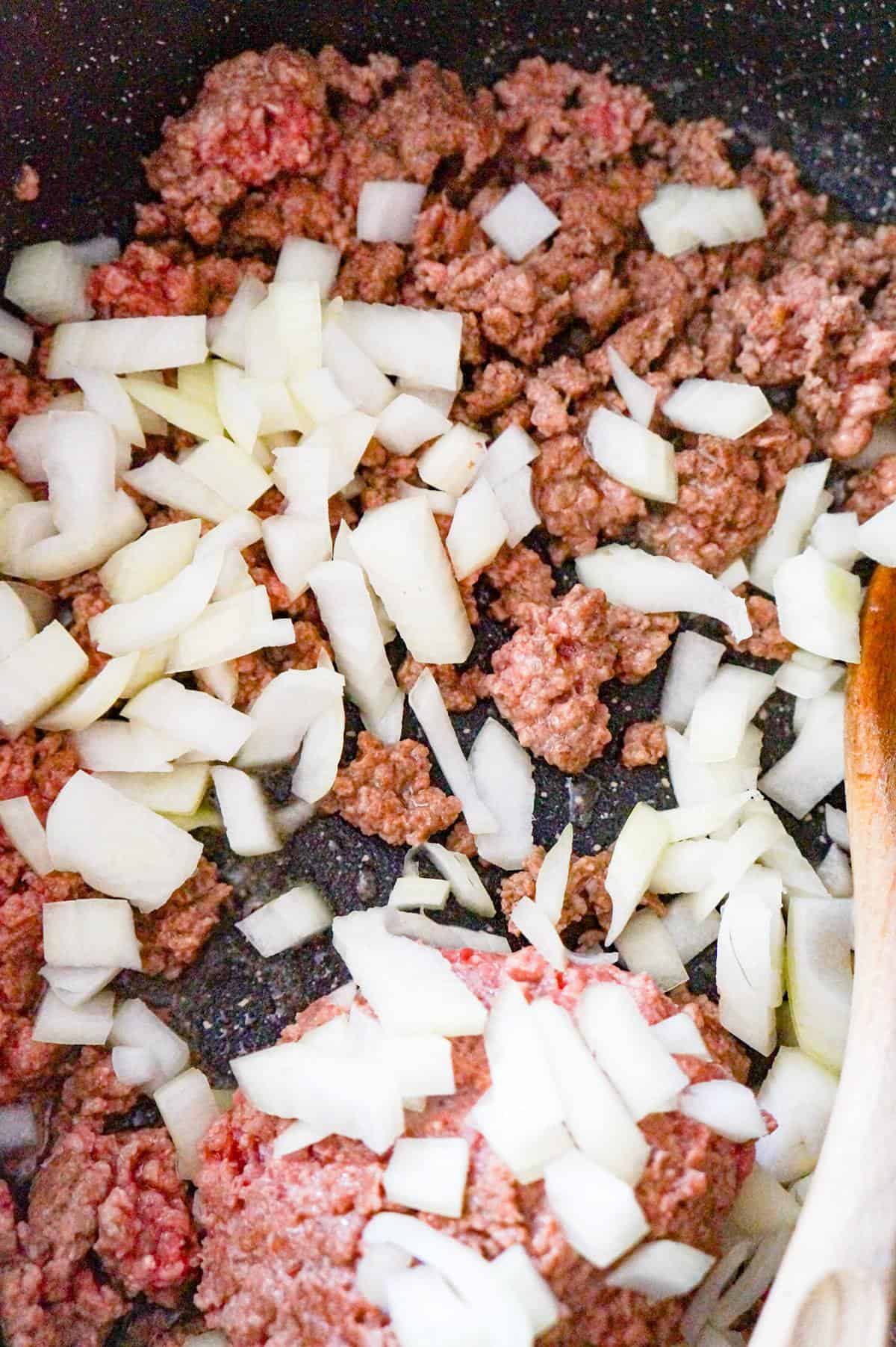 diced onions on top of ground beef in a pan