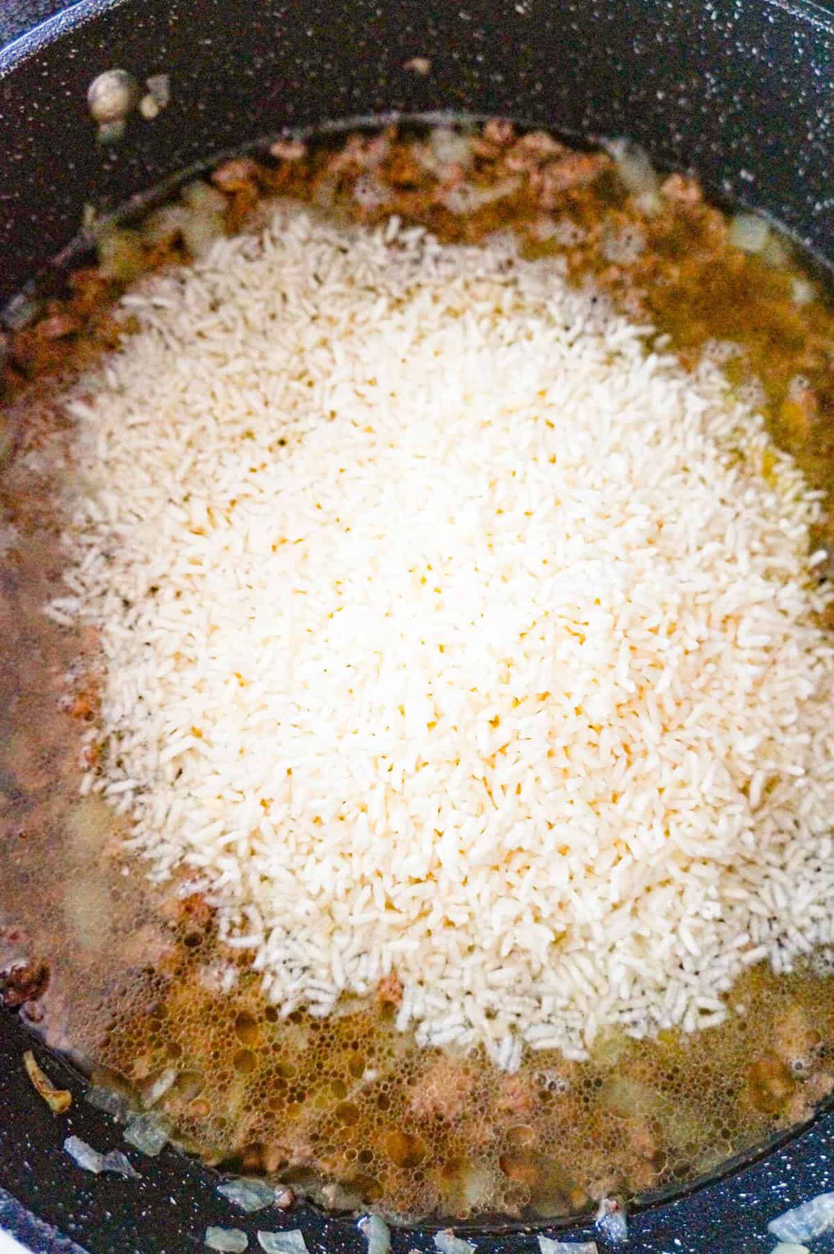 instant rice on top of cooked ground beef in broth in a pan