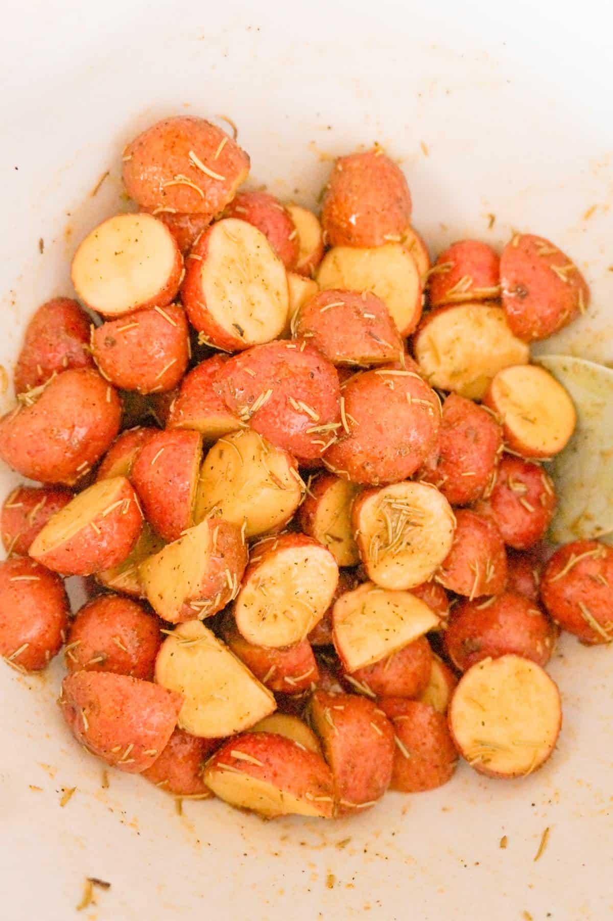 potato halves tossed in olive oil and seasonings in a mixing bowl