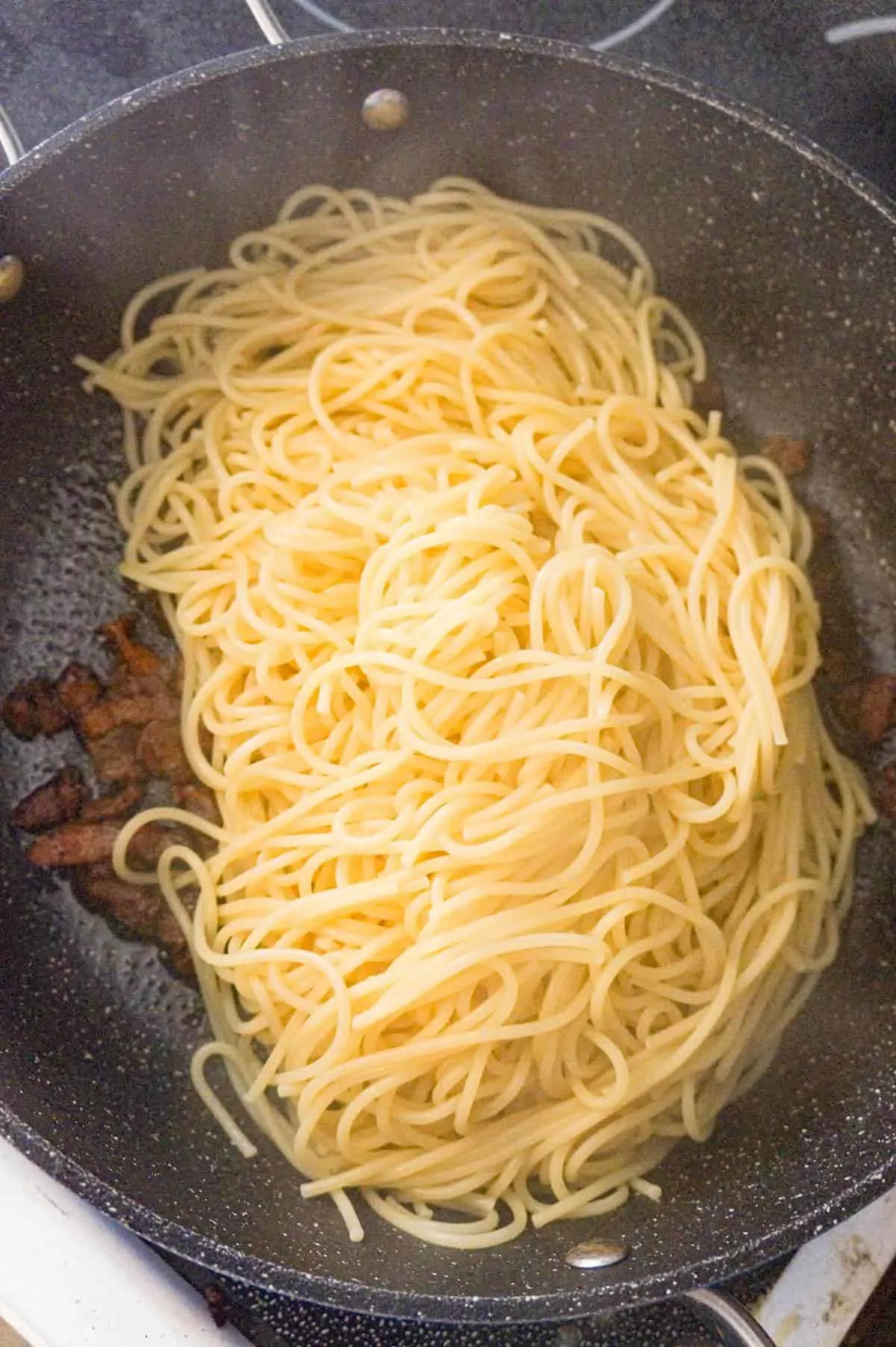 cooked spaghetti added to saute pan with cooked bacon pieces
