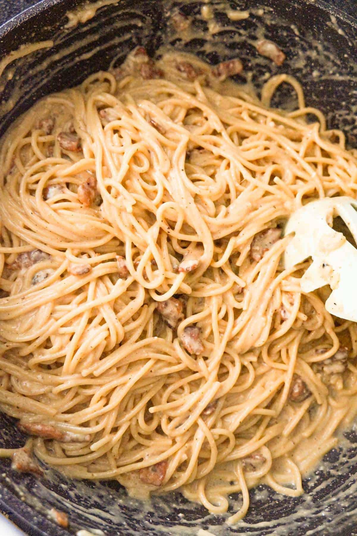 spaghetti carbonara being tossed in a saute pan