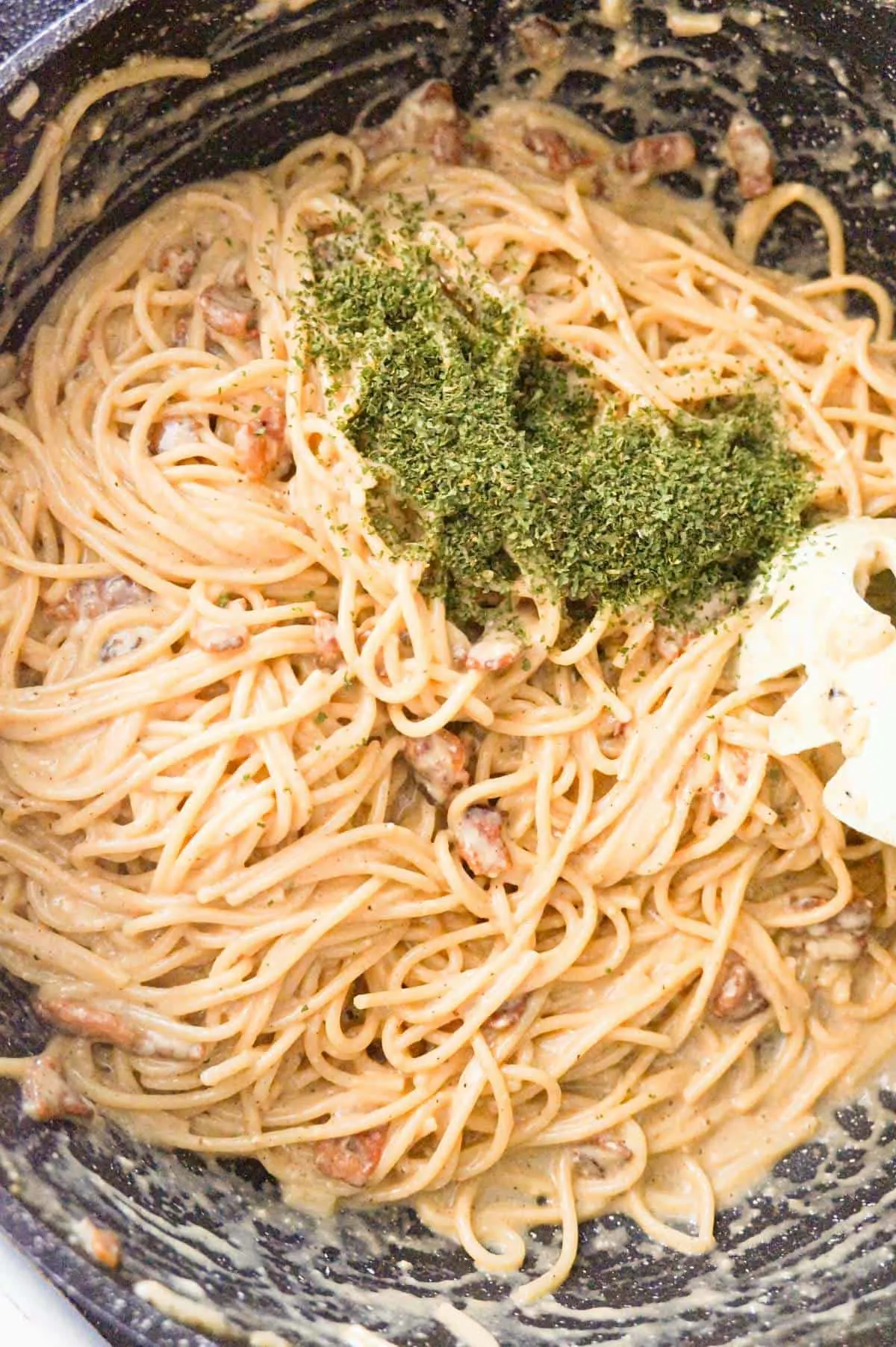 parsley flakes on top of spaghetti carbonara in a saute pan