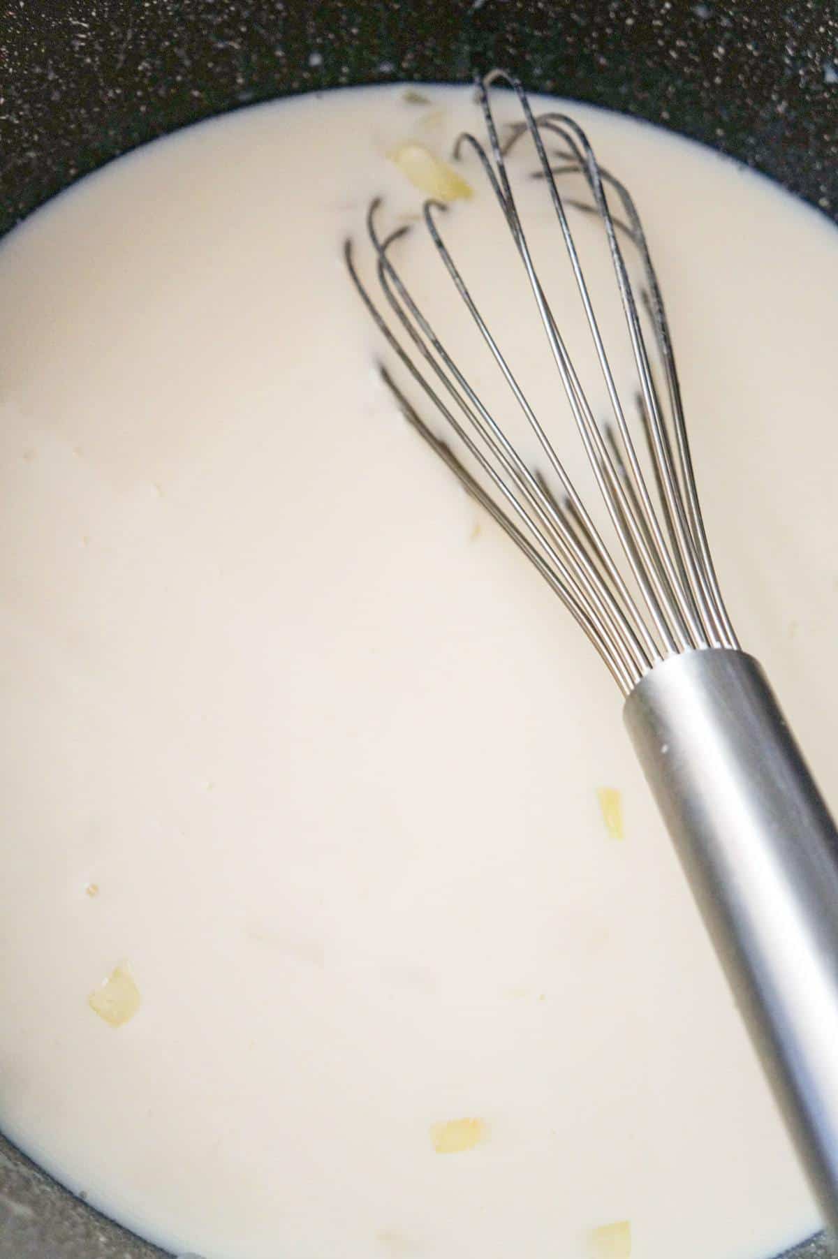 milk and chicken broth mixture being whisked in a large pot