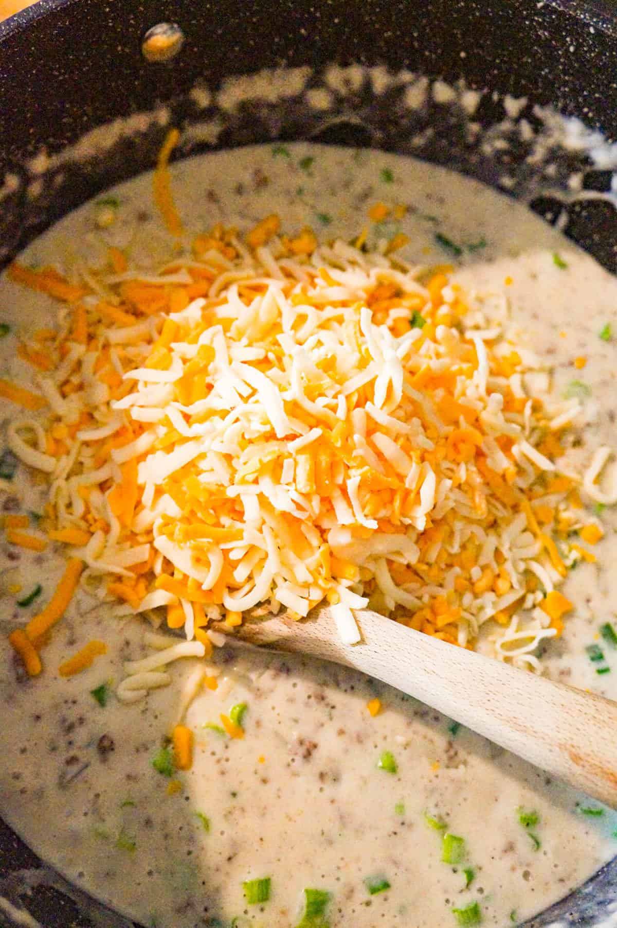 shredded cheddar cheese on top of hamburger potato soup in a large pot