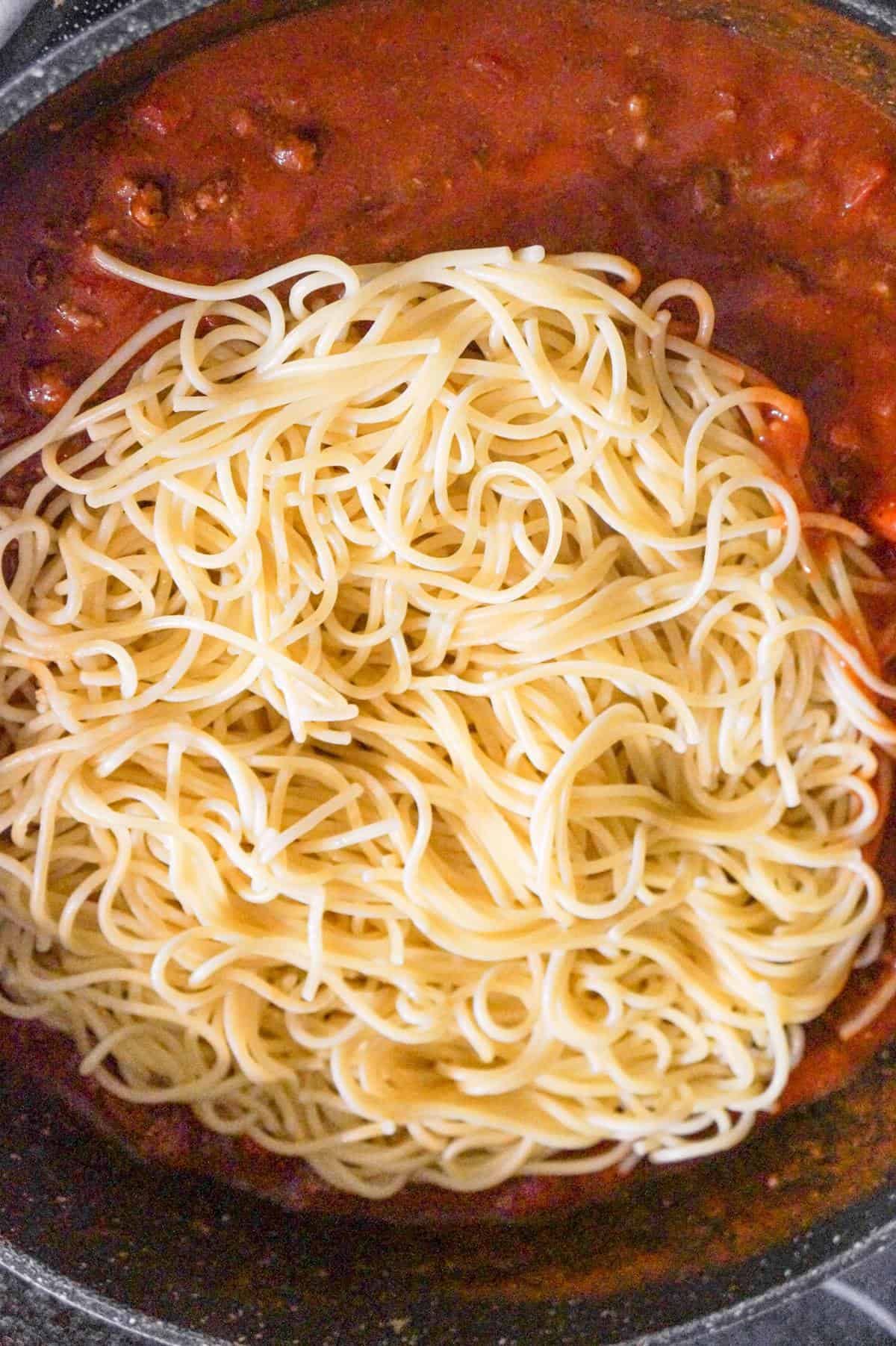 cooked spaghetti on top of ground beef and tomato sauce in a pan