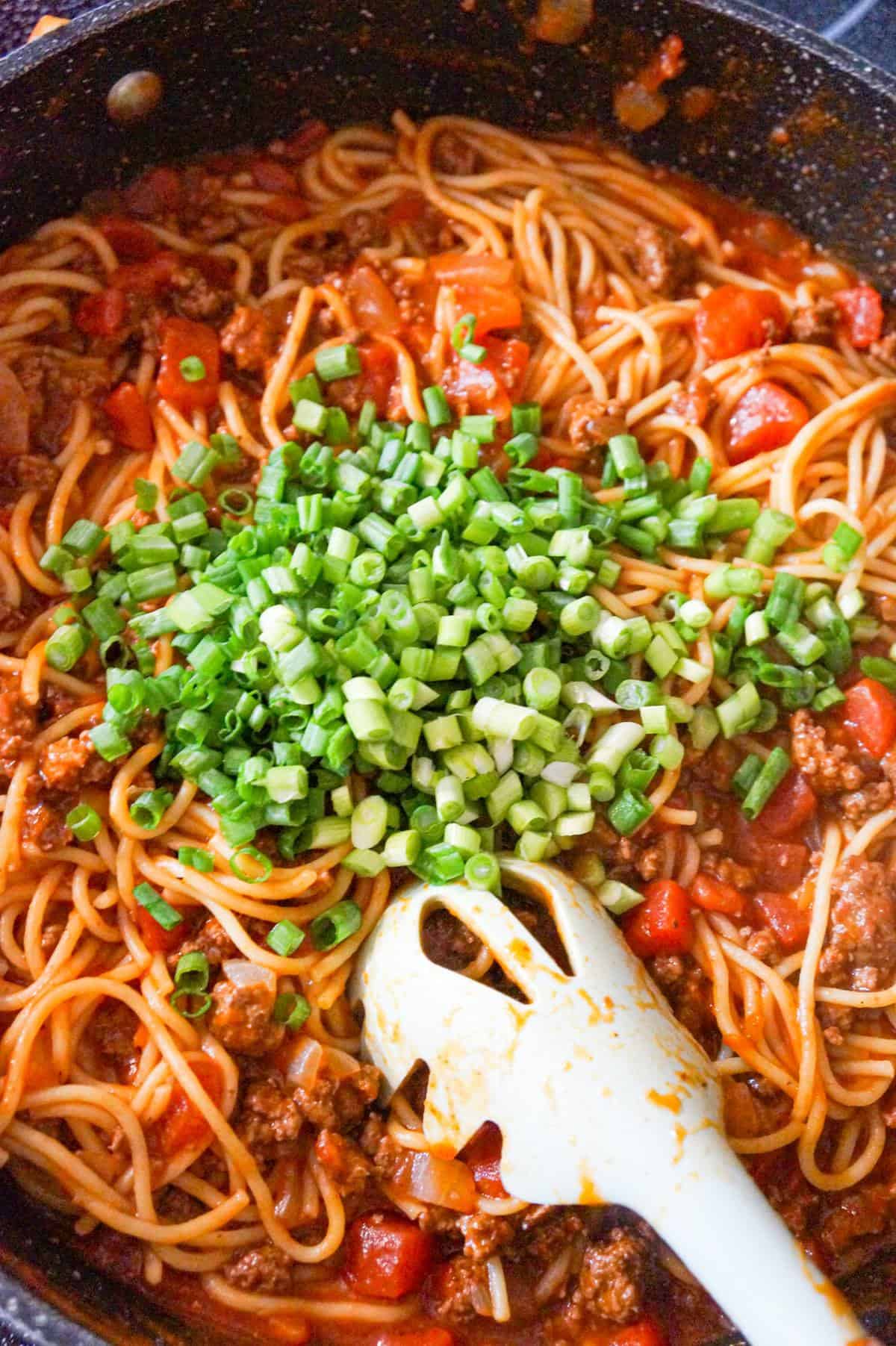 chopped green onions on top of taco spaghetti in a pan