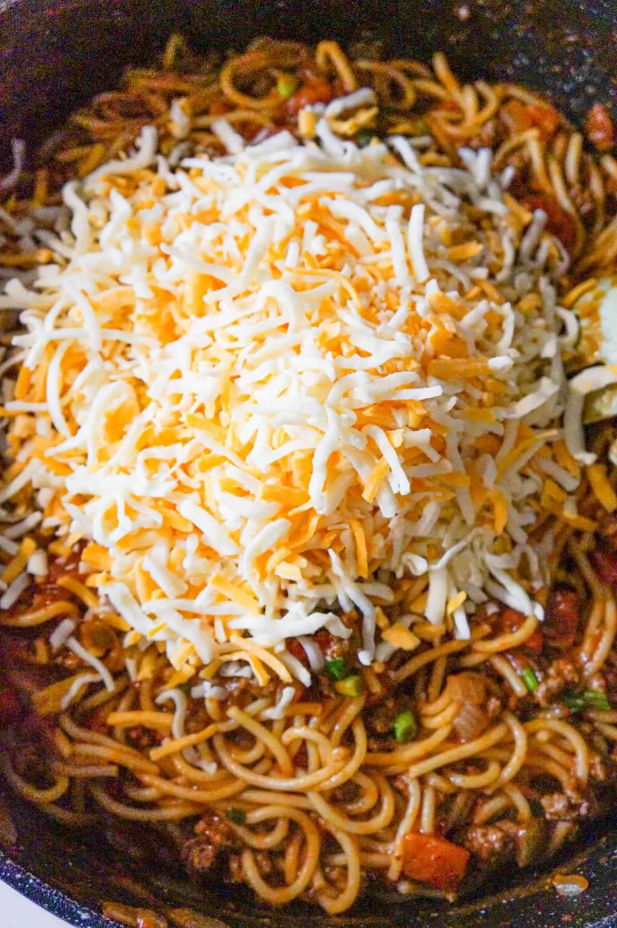 shredded cheese on top of taco spaghetti in pan