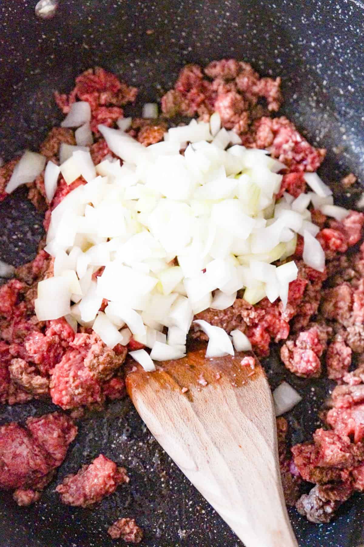 diced onions on top of ground beef in a saute pan
