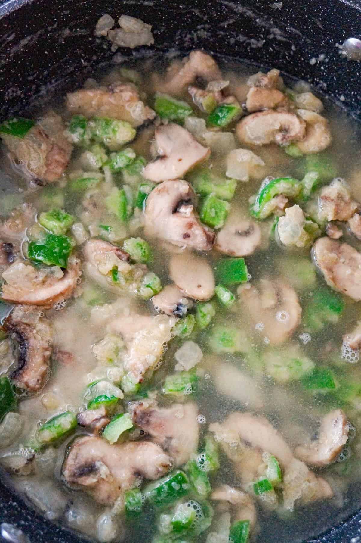 sliced mushrooms, diced onions and diced green peppers coated in flour cooking in a saute pan