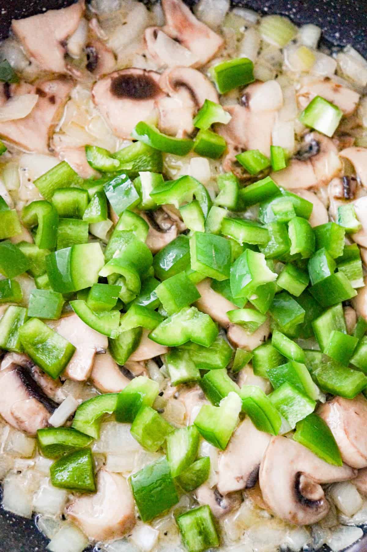 diced green peppers on top of sliced mushrooms and diced onions in a saute pan