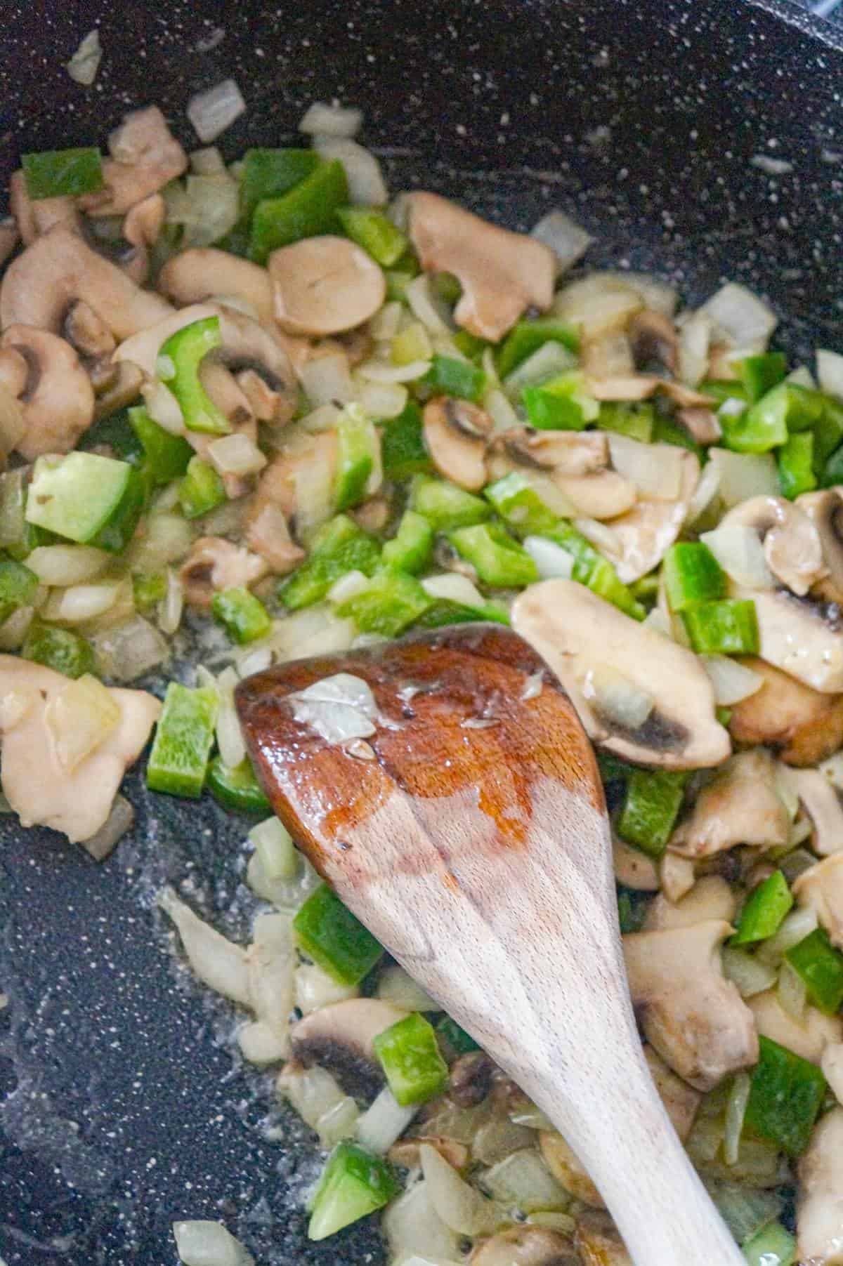 sliced mushrooms, diced onions and diced green peppers cooking in a saute pan