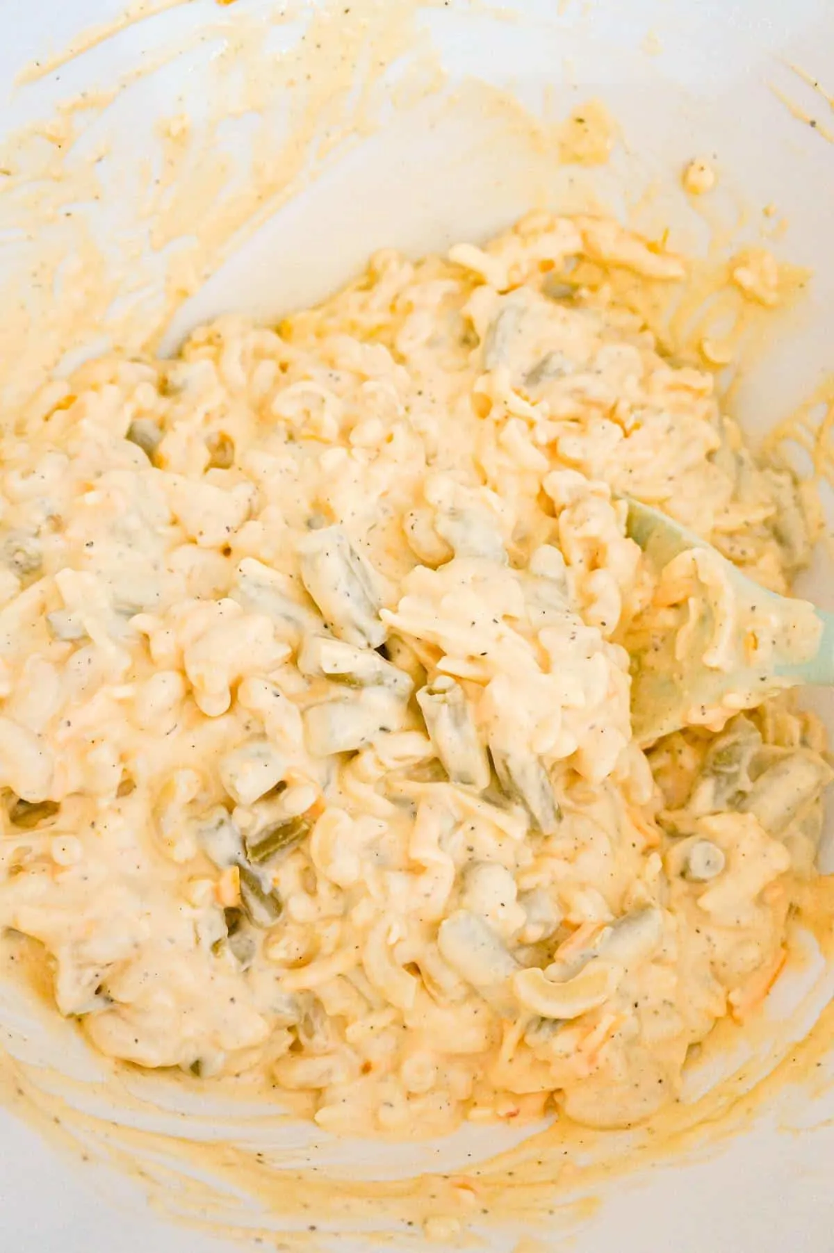 creamy macaroni and cheese mixture with green beans in a mixing bowl
