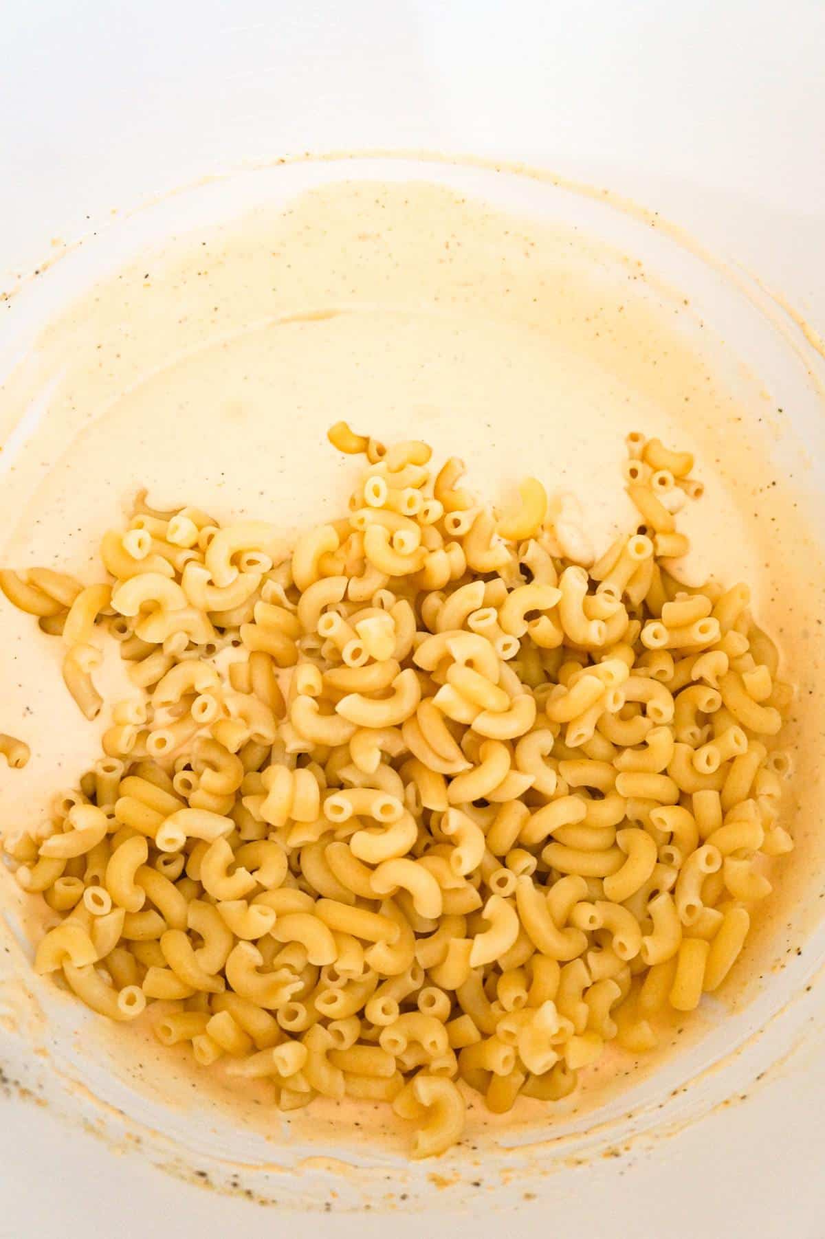 cooked macaroni noodles on top of heavy cream and cheddar soup mixture in a mixing bowl