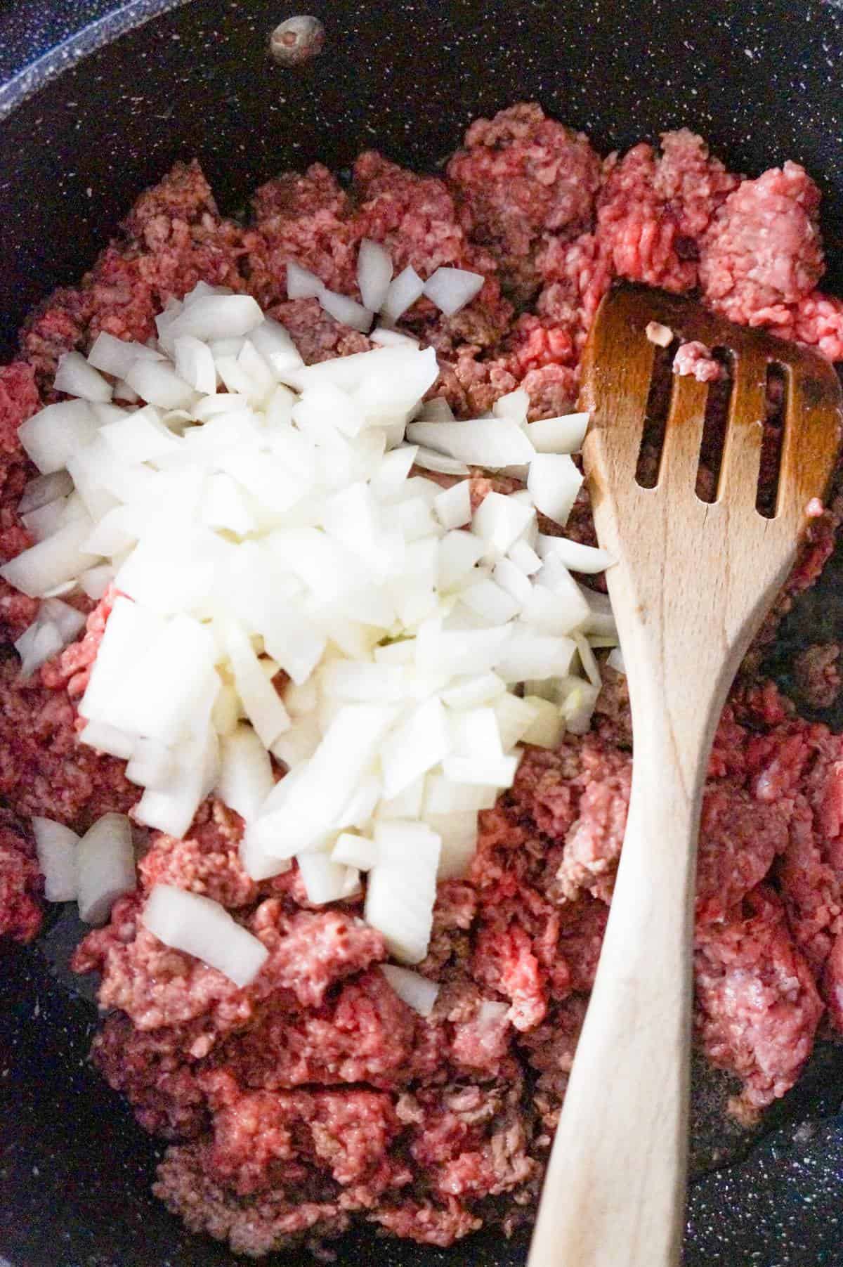 diced onions on top of raw ground beef in a saute pan