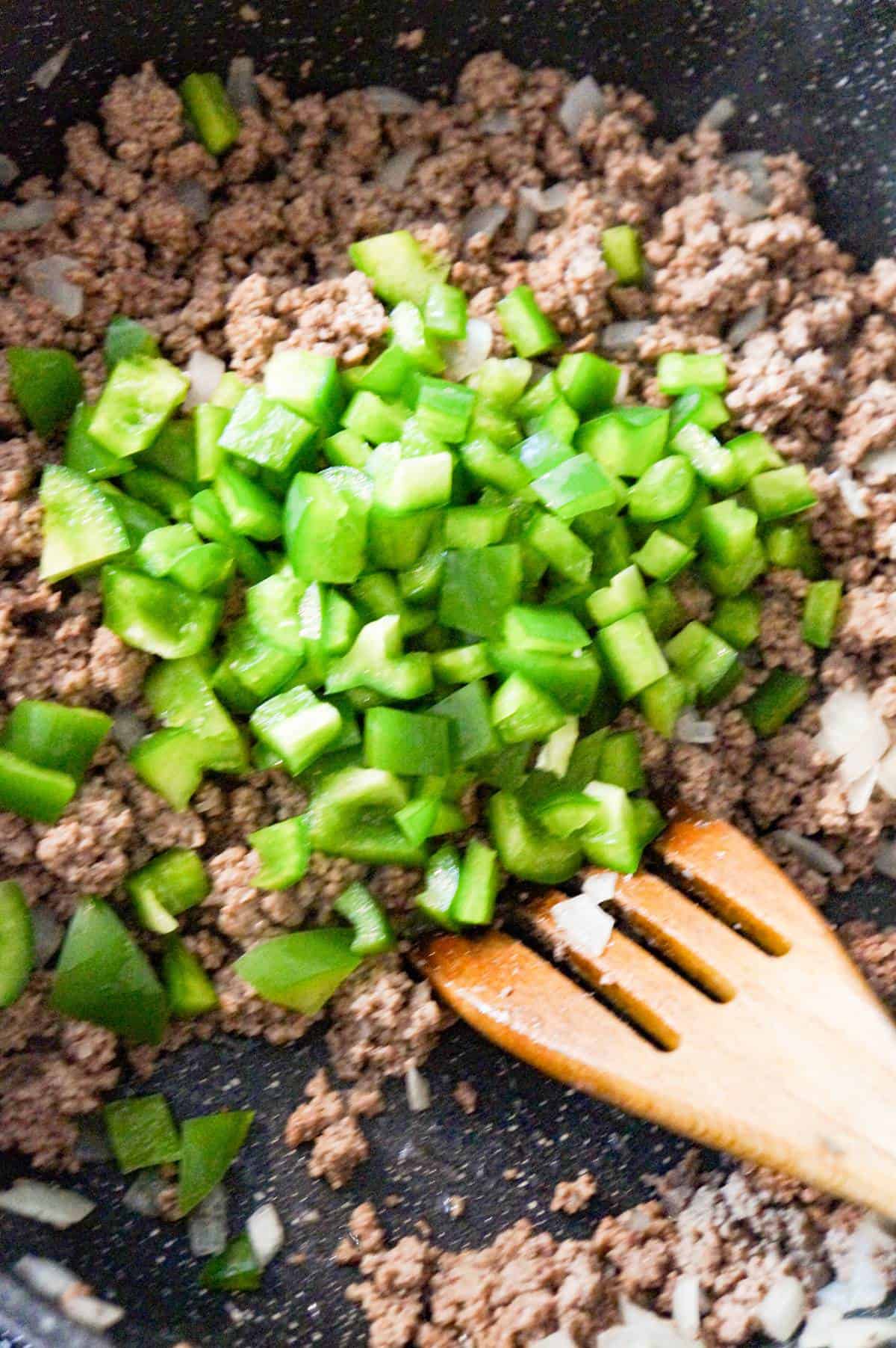 diced green peppers on top of cooked ground beef in a saute pan