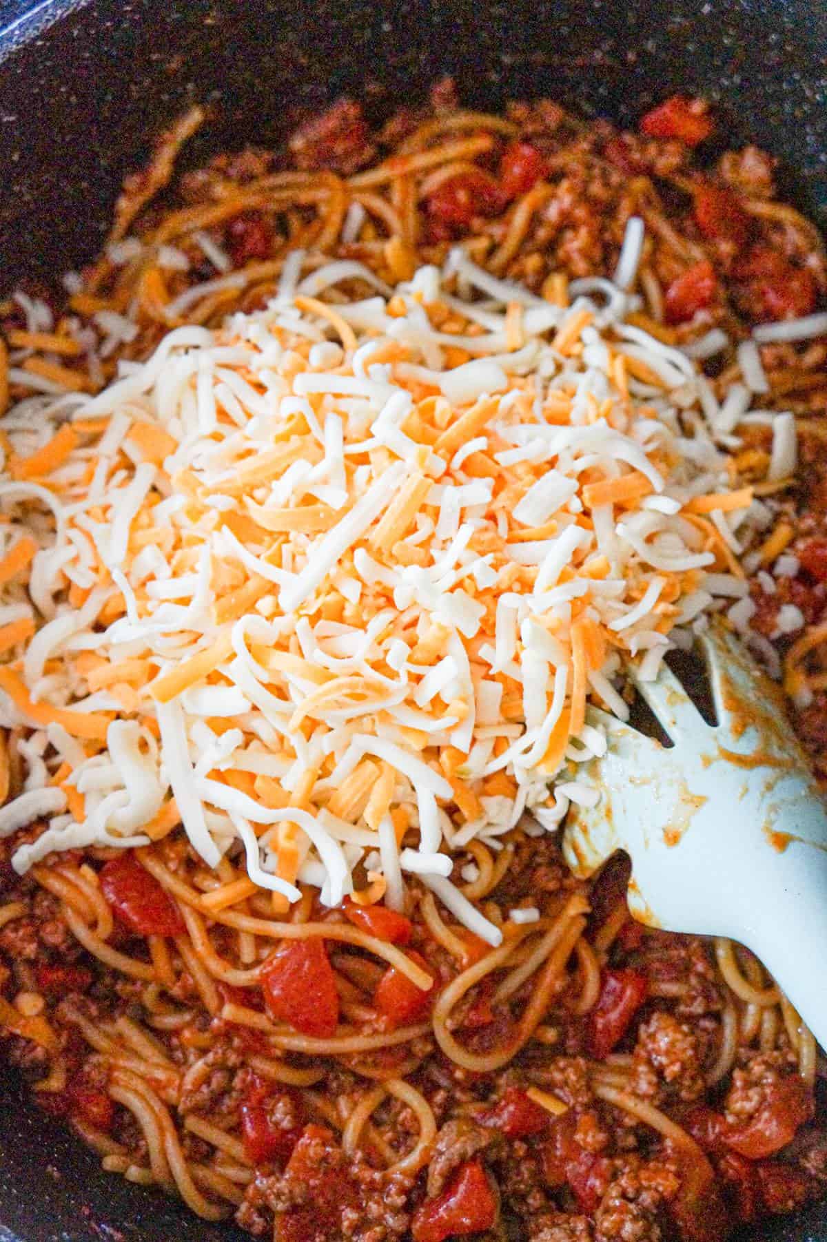 shredded cheese on top of spaghetti with ground beef in a saute pan
