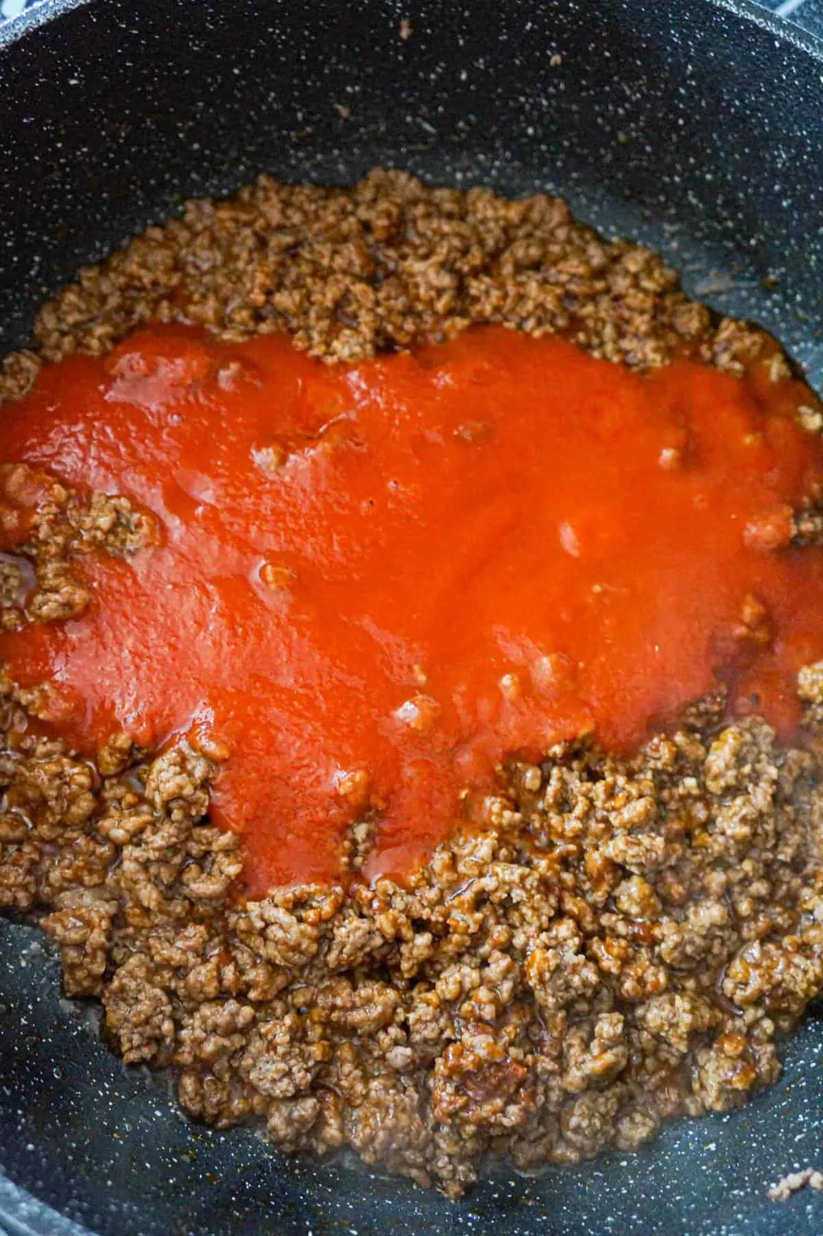 tomato sauce on top of cooked ground beef and taco seasoning in a saute pan