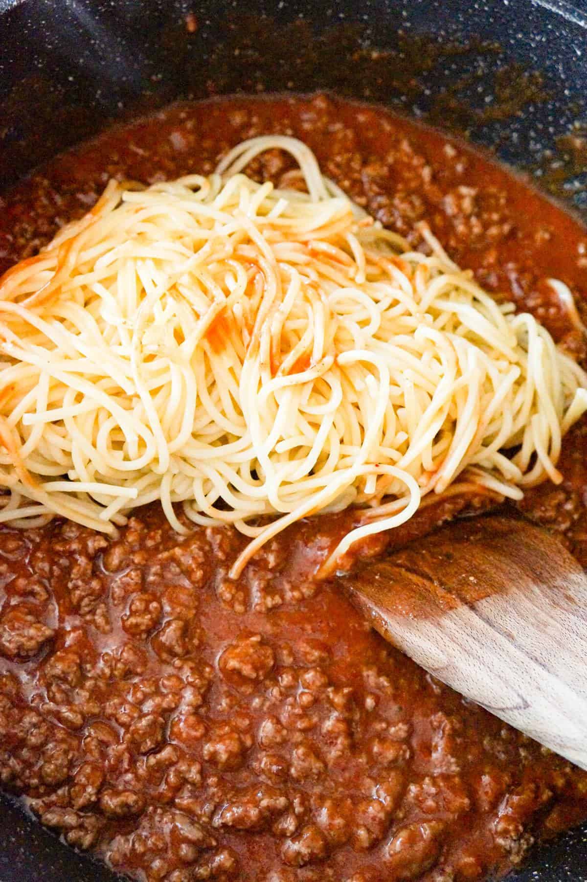cooked spaghetti on top of ground beef and tomato sauce in a saute pan