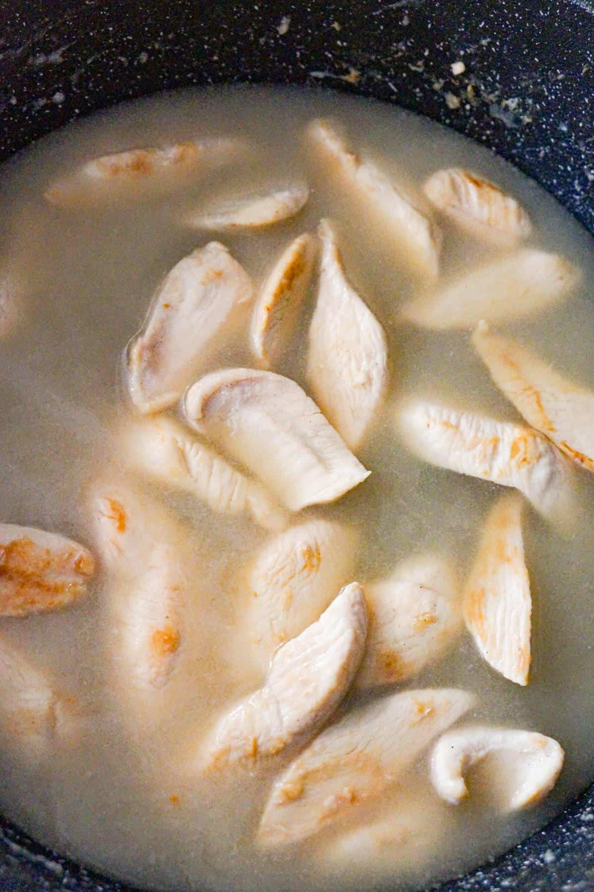 cooked chicken breast strips in broth in a saute pan