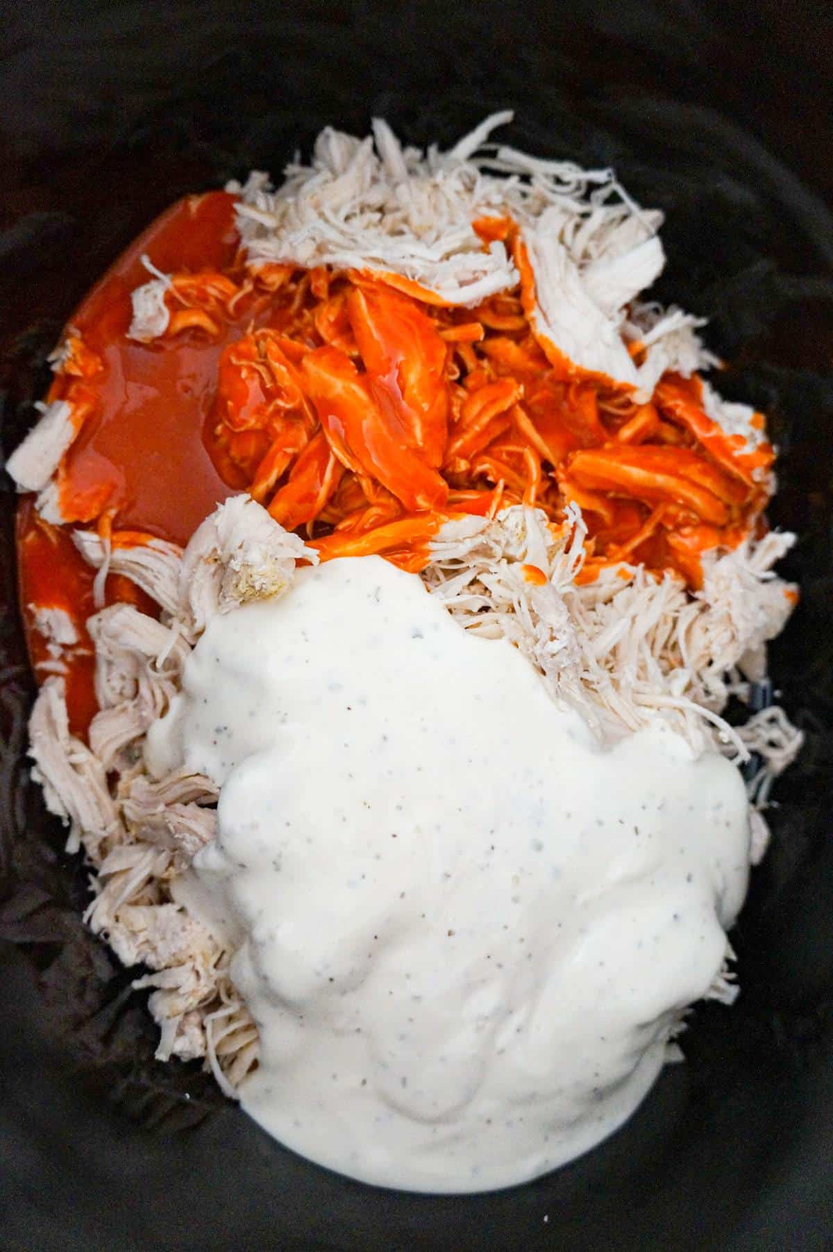 ranch dressing and buffalo sauce on top of shredded chicken in a crock pot