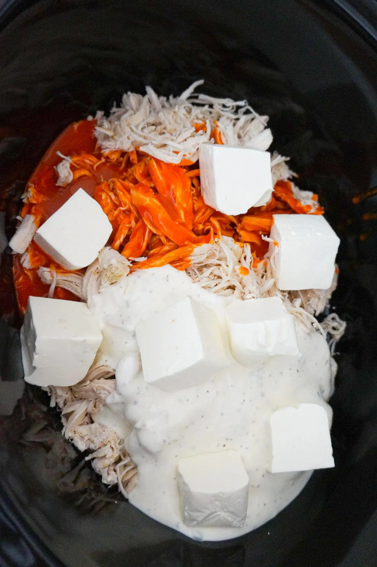 cubes of cream cheese on top of shredded chicken, buffalo sauce and ranch sauce in a crock pot