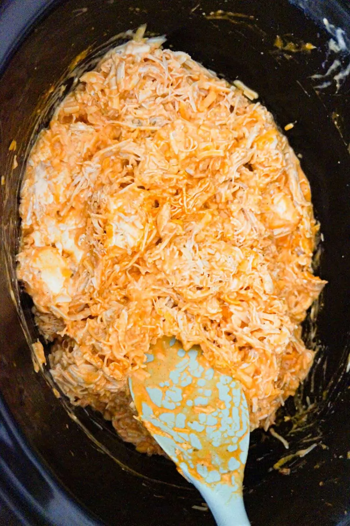 buffalo chicken dip being stirred during cooking in a crock pot