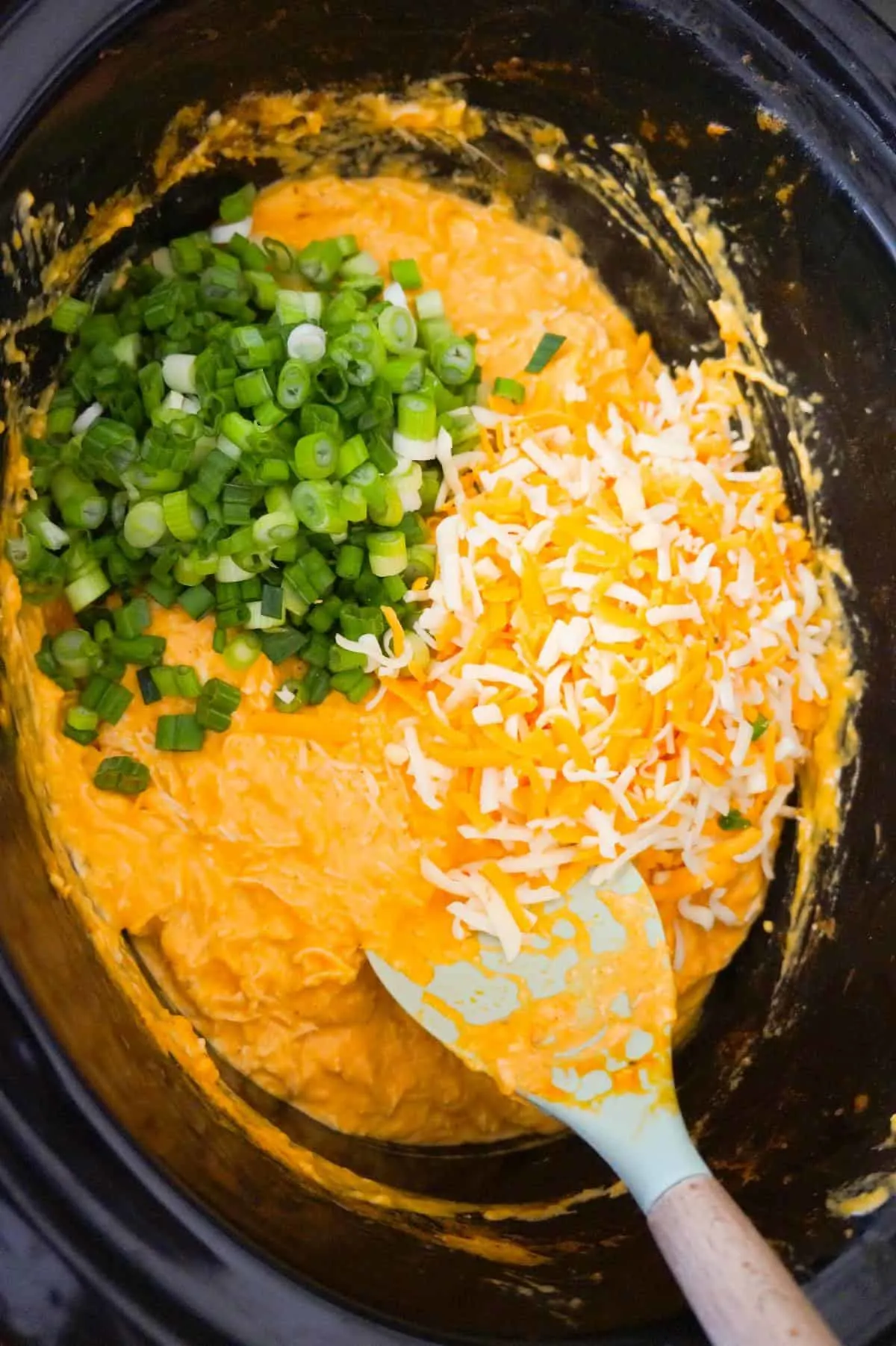 shredded cheese and chopped green onions on top of Buffalo chicken dip