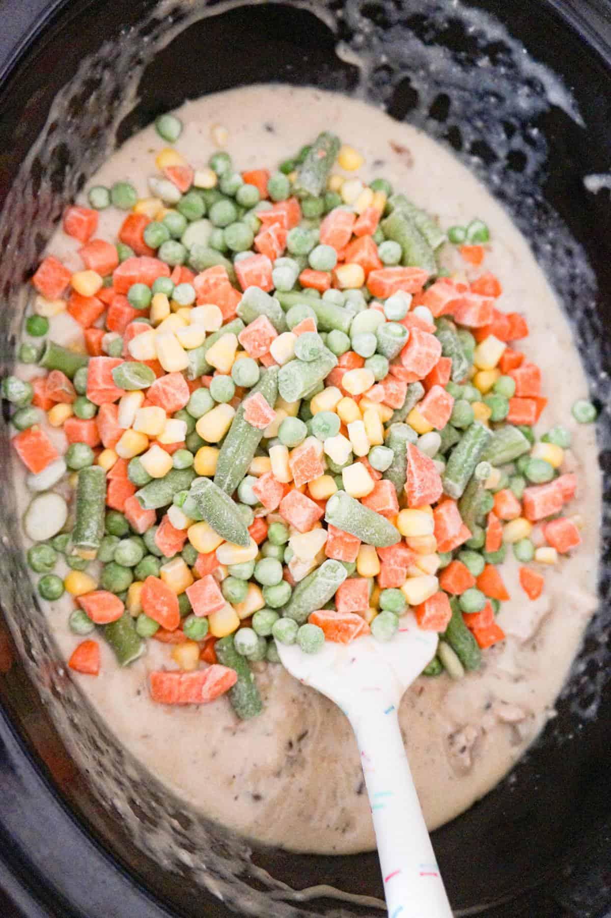 frozen mixed veggies on top of a creamy chicken mixture in a crock pot