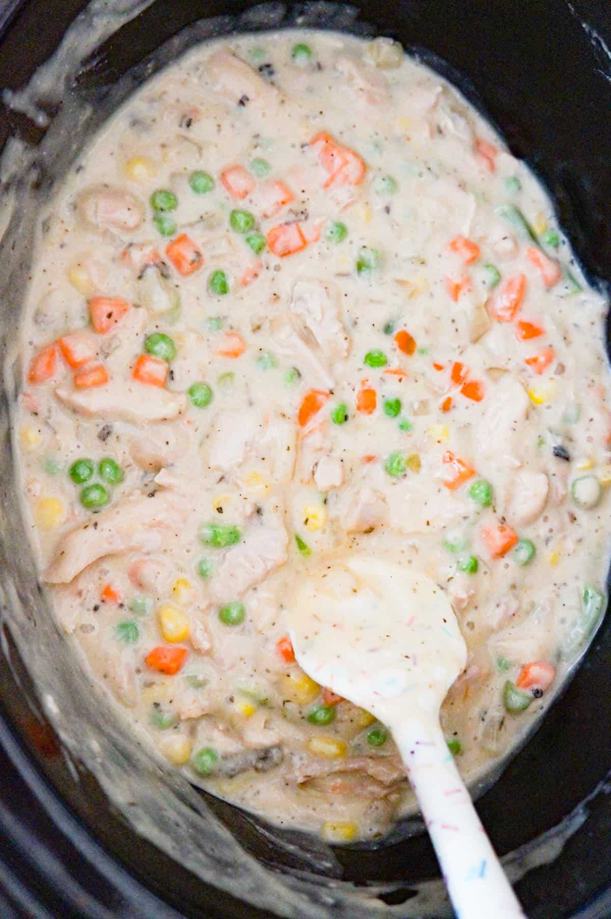 vegetables being stirred into a creamy chicken mixture in a crock pot