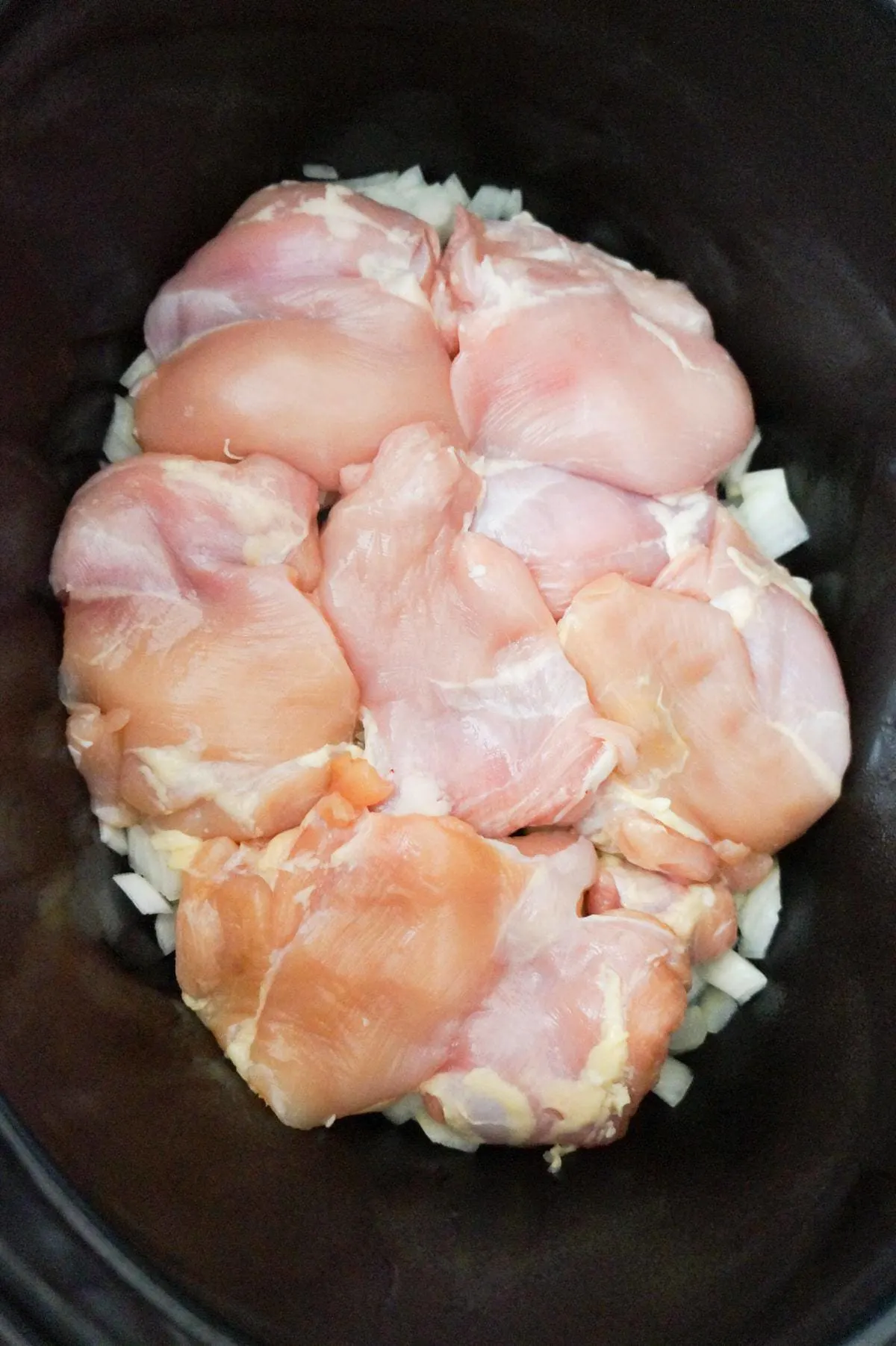 raw chicken thighs on top of diced onions in a crock pot