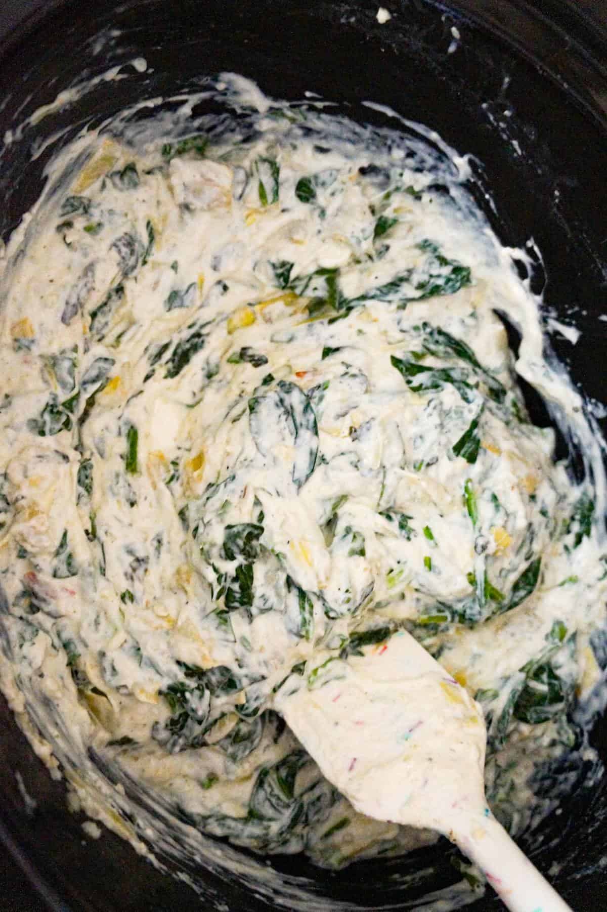 stirring spinach and artichoke dip in a crock pot