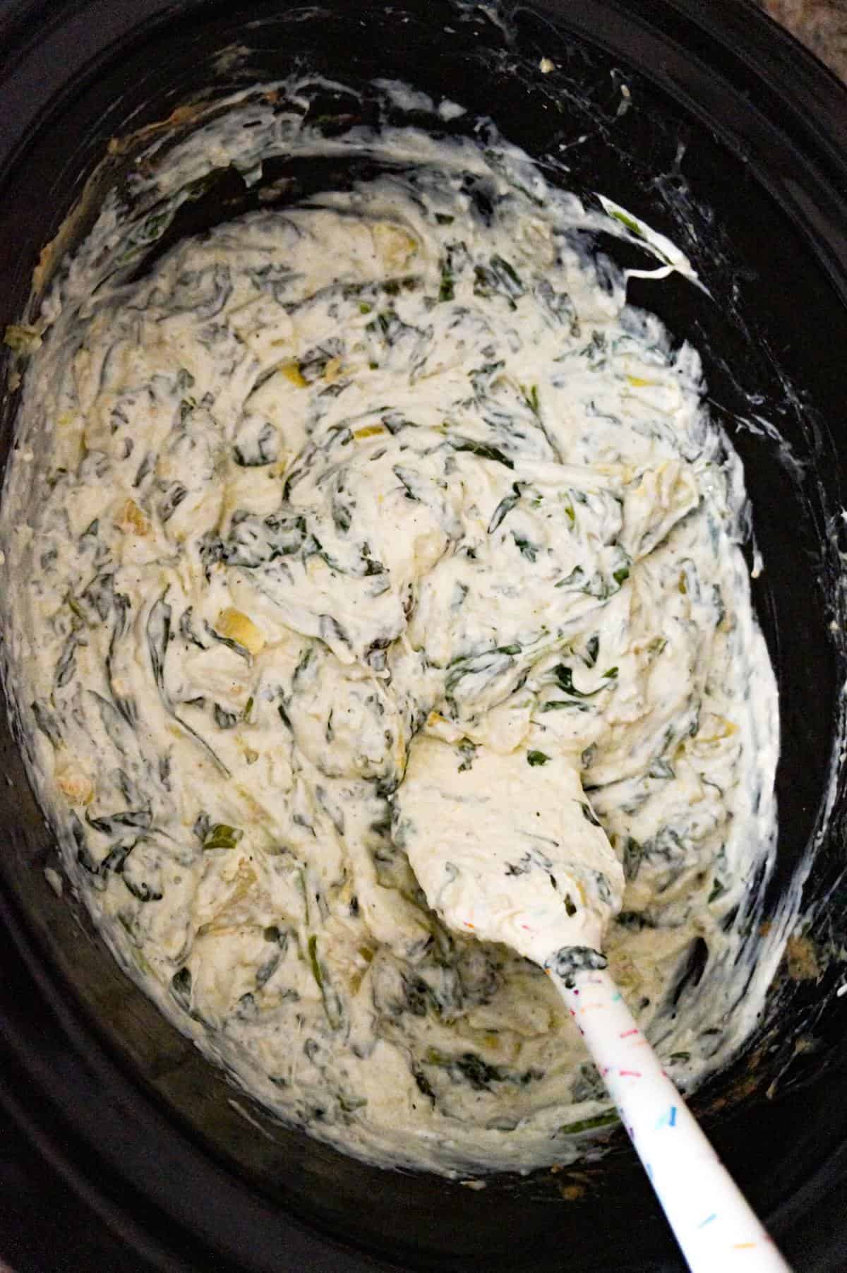 slow cooker spinach artichoke dip being stirred