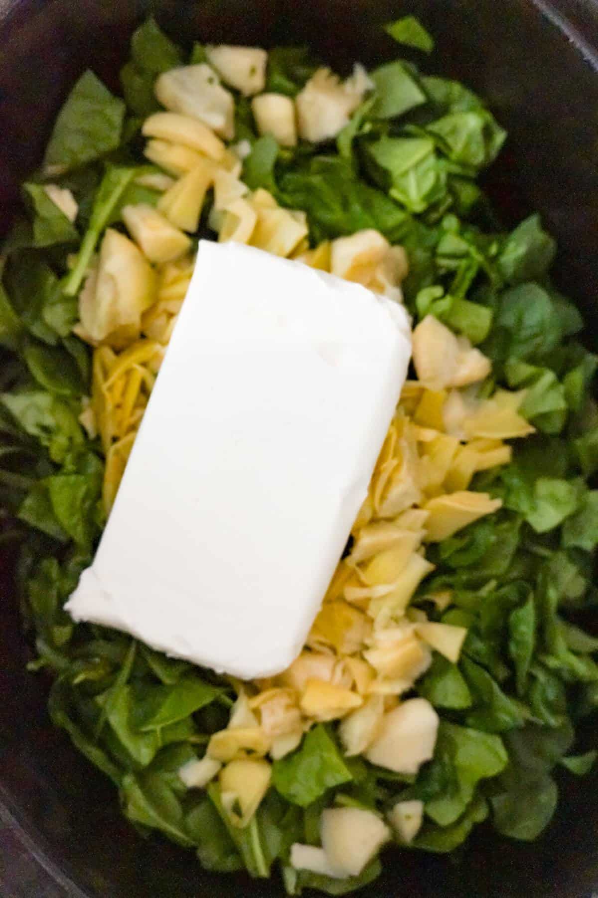 cream cheese on top of chopped artichoke and chopped spinach in a slow cooker