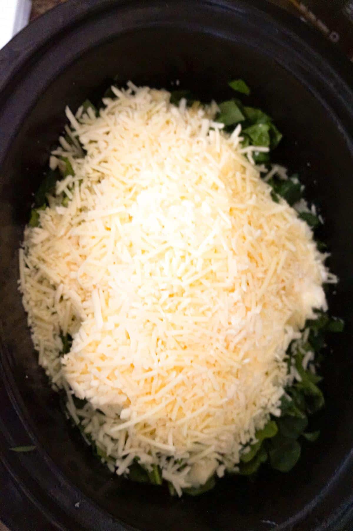 shredded mozzarella cheese and shredded Parmesan cheese on top of spinach, cream cheese and sour cream in a slow cooker