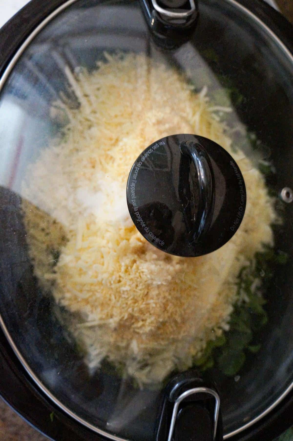 lid on crock pot full of spinach and artichoke dip ingredients