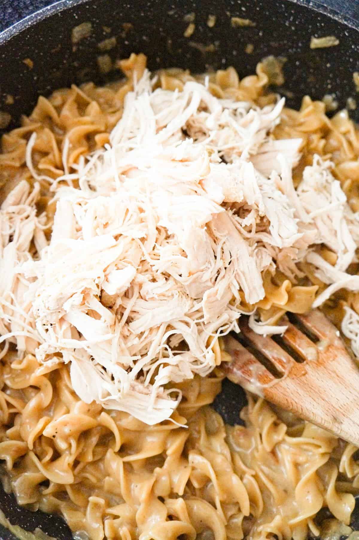 shredded chicken on top of cooked egg noodles in a pot