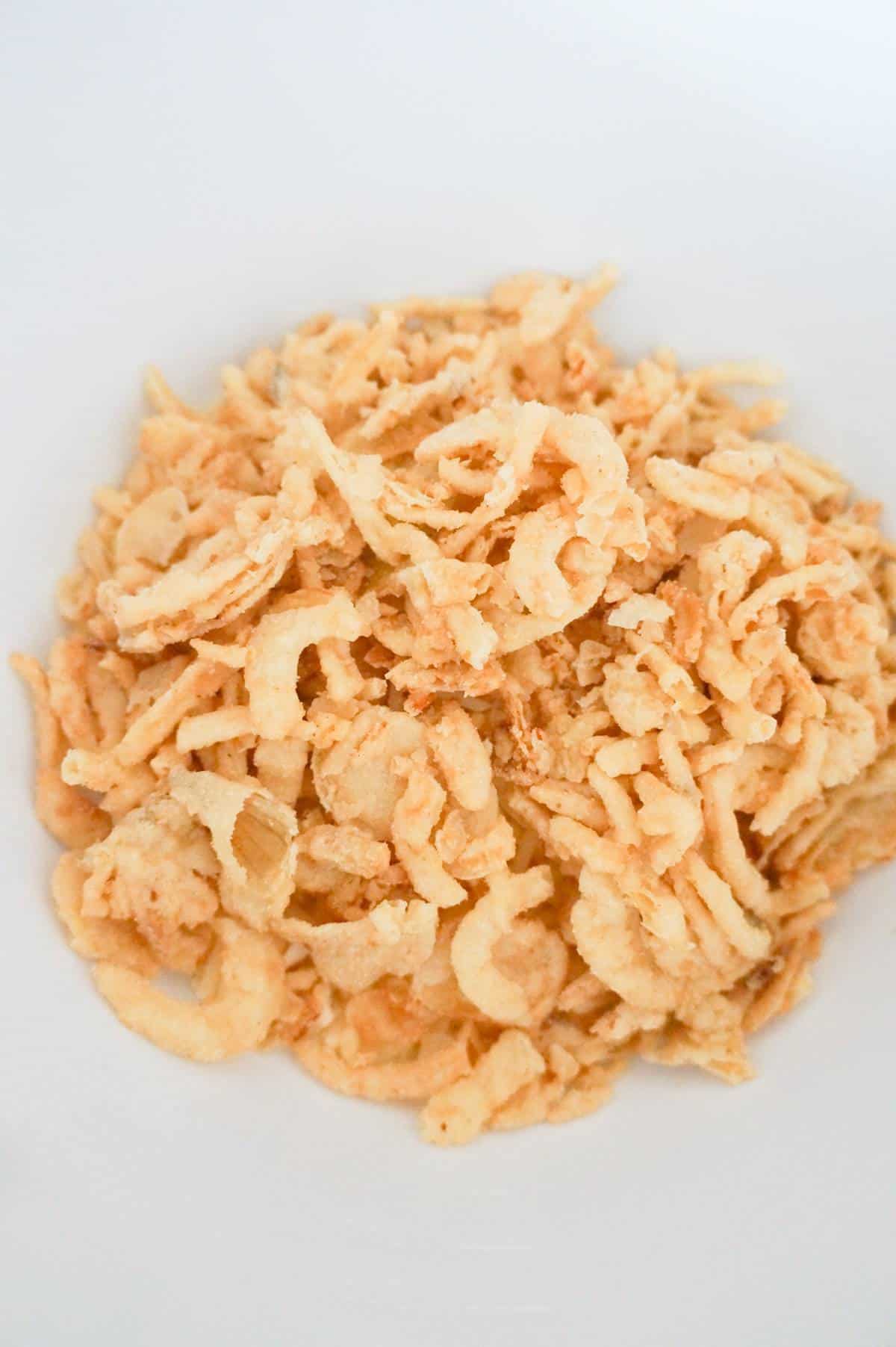 crispy fried onions on top of shredded cheese in a mixing bowl