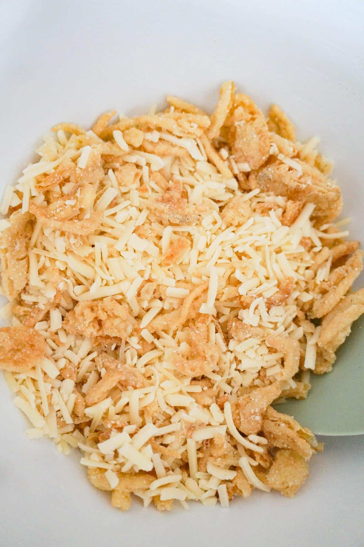 shredded cheese and crispy fried onions in a mixing bowl