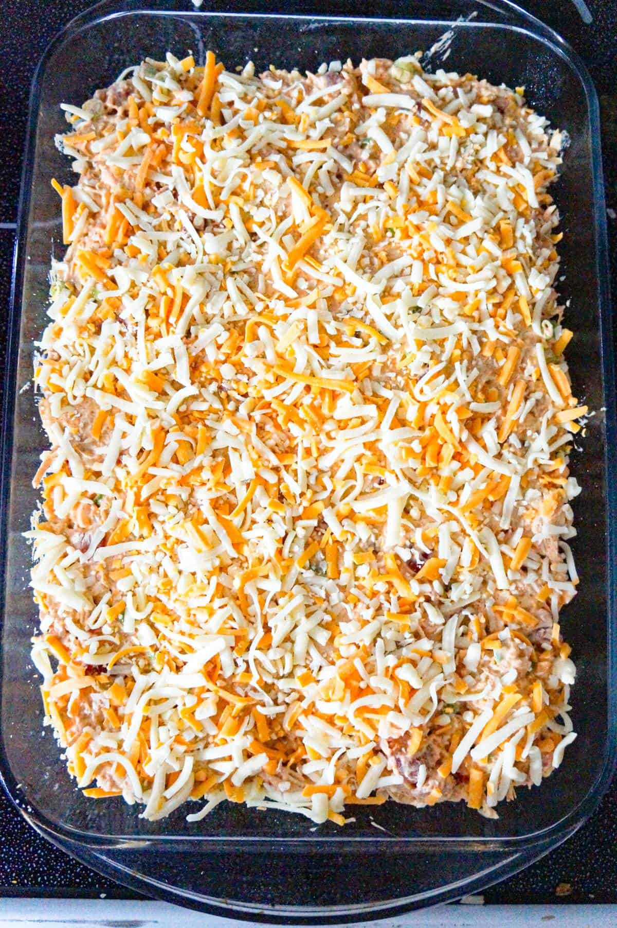 shredded cheese on top of chicken mixture in a casserole dish