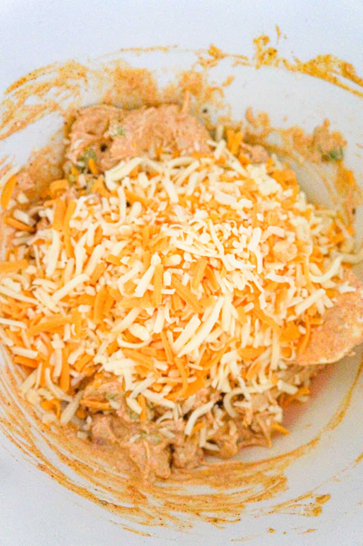 shredded cheese on top of chicken mixture in a mixing bowl