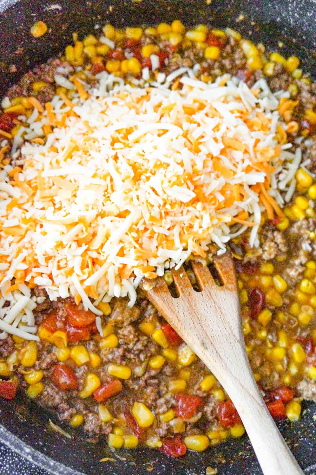 shredded cheese on top of ground beef mixture in a saute pan