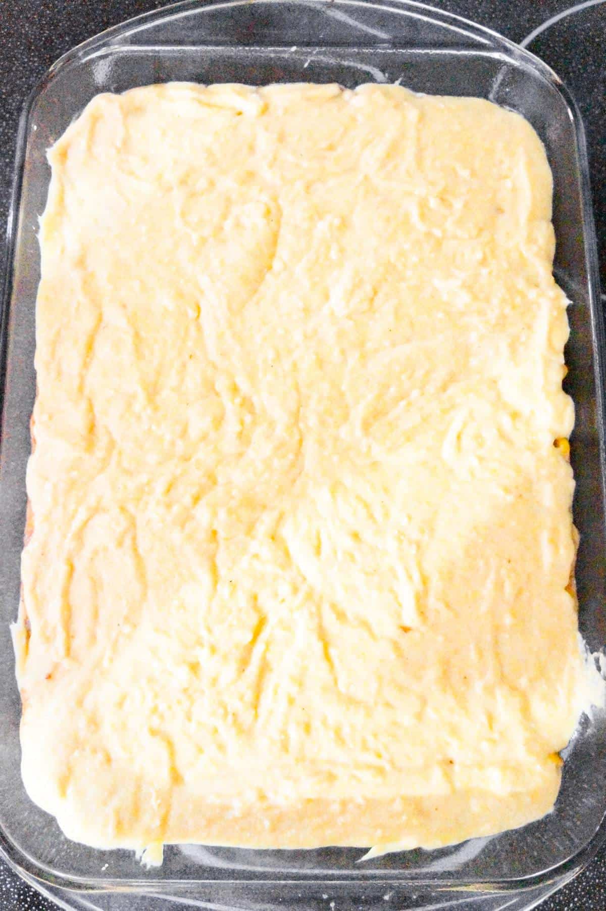 cornbread batter on top of casserole in a baking dish