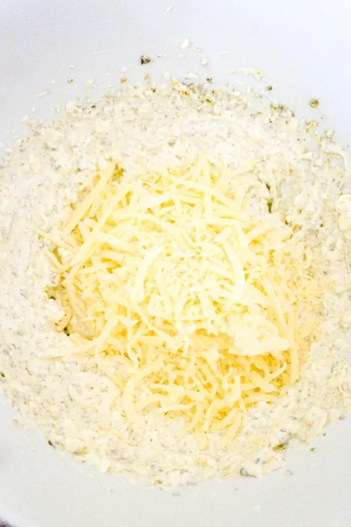 shredded Italian cheeses on top of sour cream and cream cheese mixture in a mixing bowl