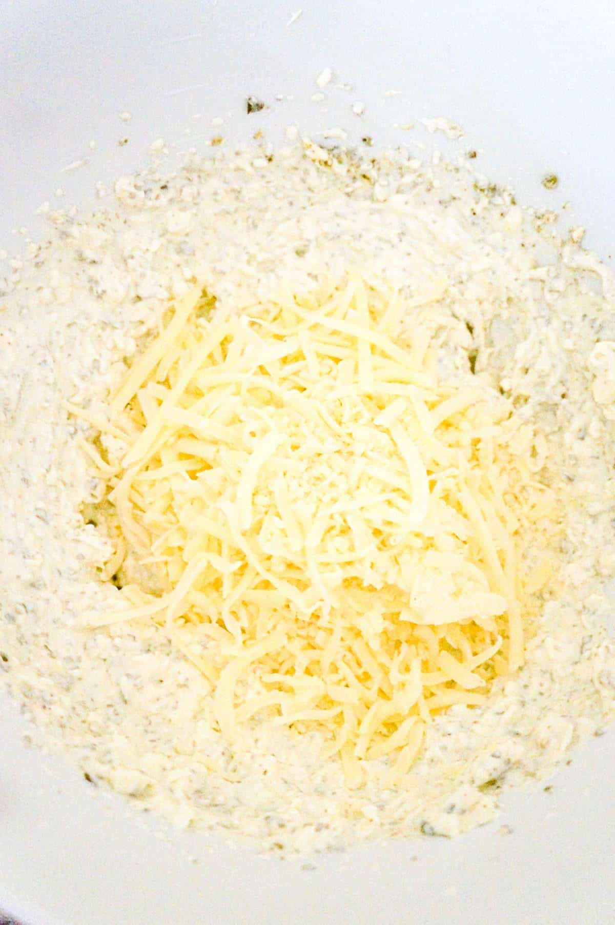 shredded Italian cheeses on top of sour cream and cream cheese mixture in a mixing bowl
