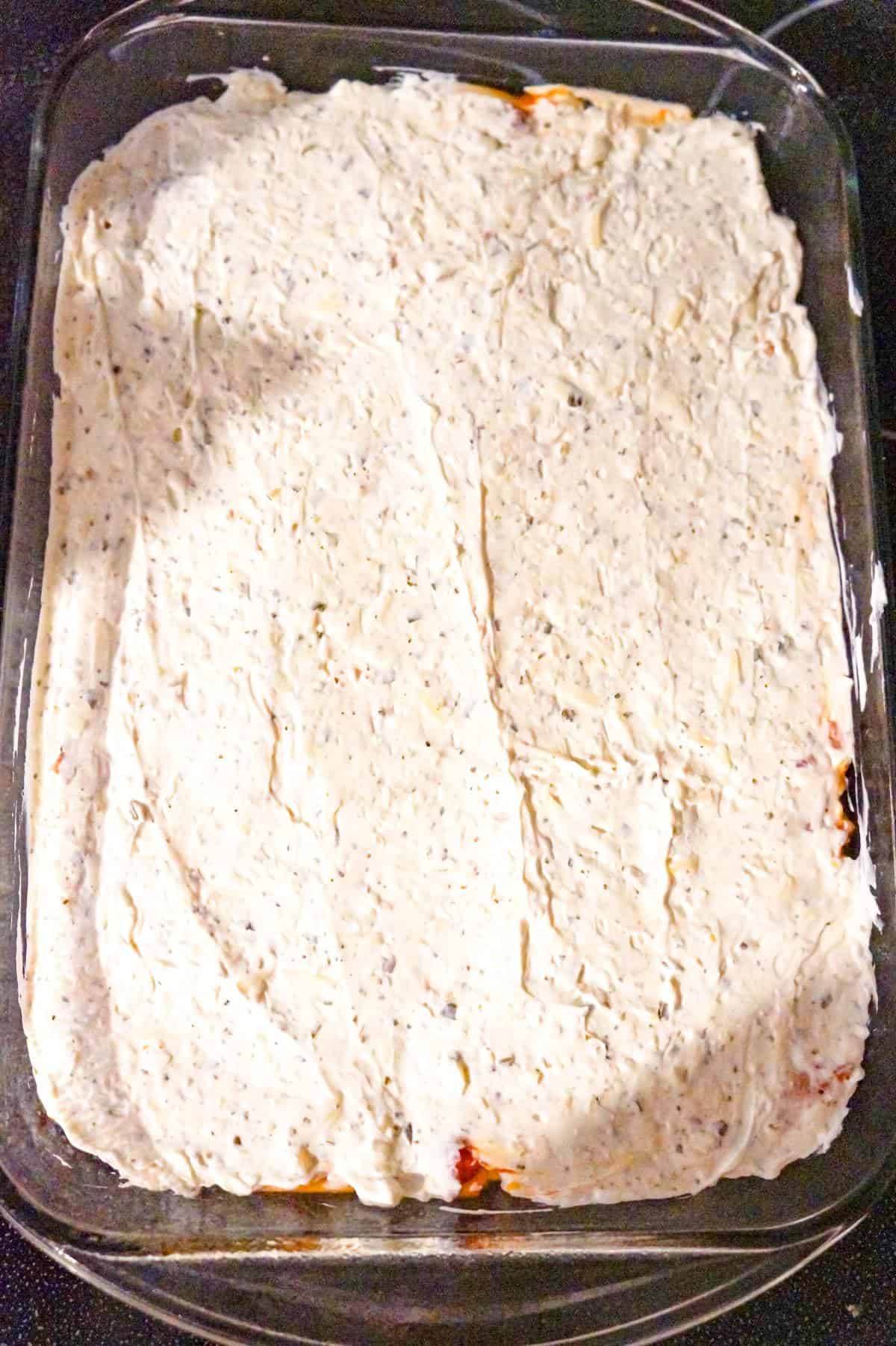 cream cheese and sour cream mixture on top of spaghetti in a baking dish