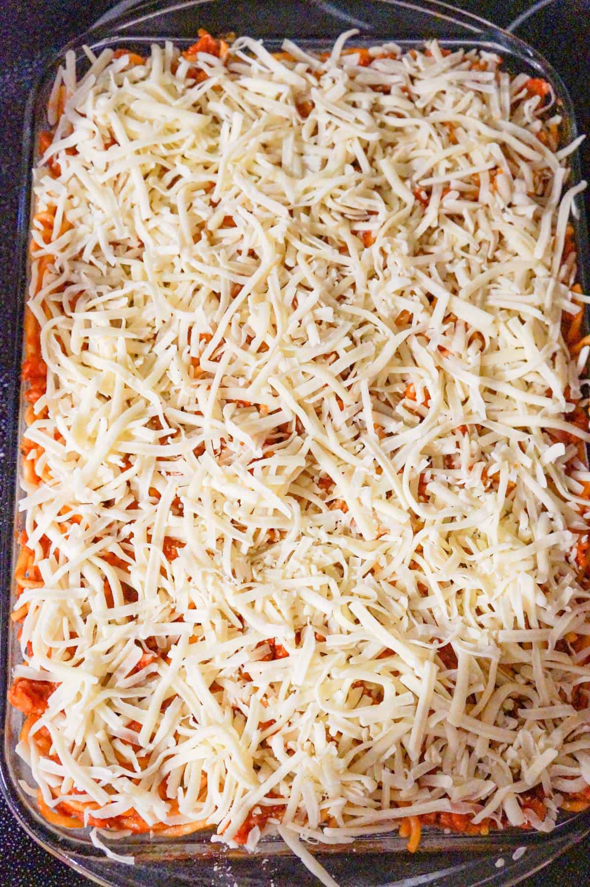 shredded cheese on top of spaghetti in a baking dish