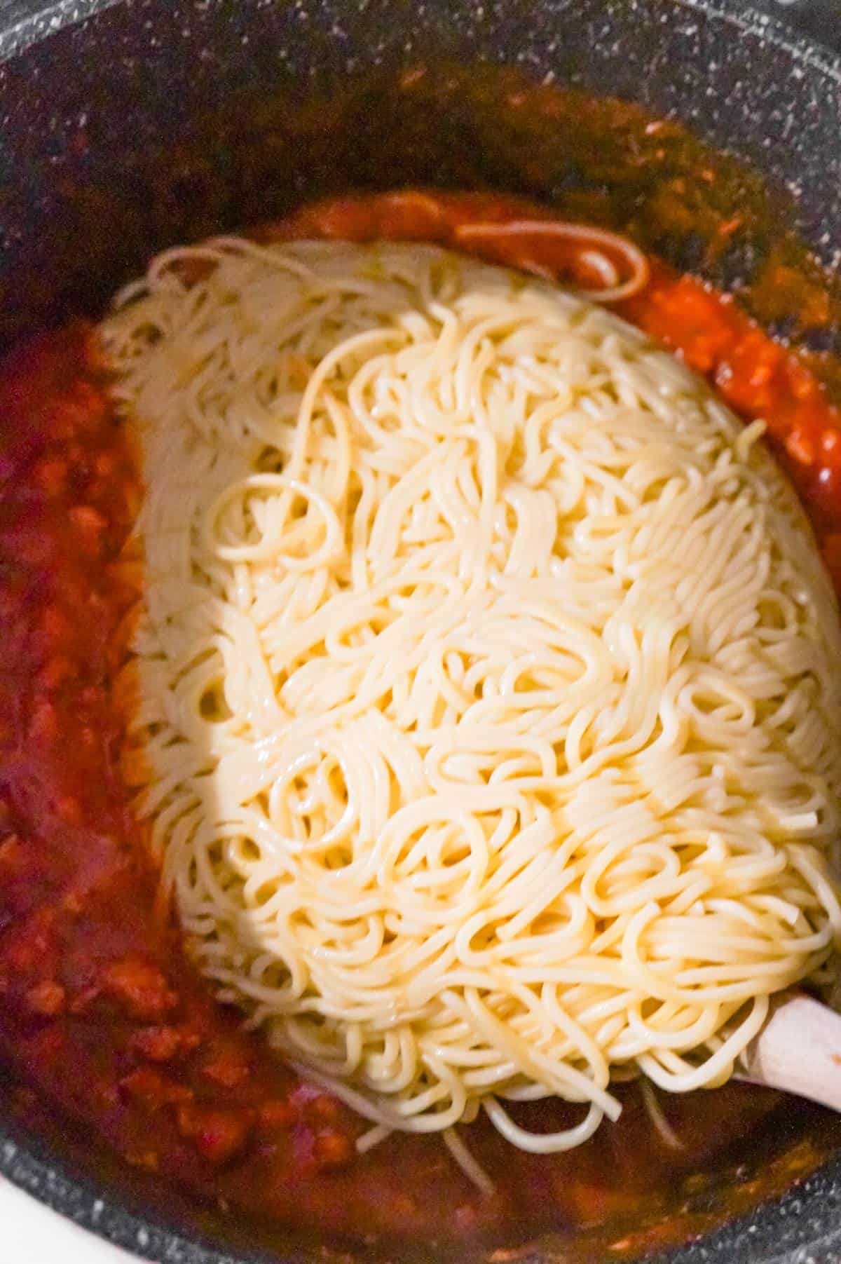 cooked spaghetti on top of marinara and ground sausage in a large pot